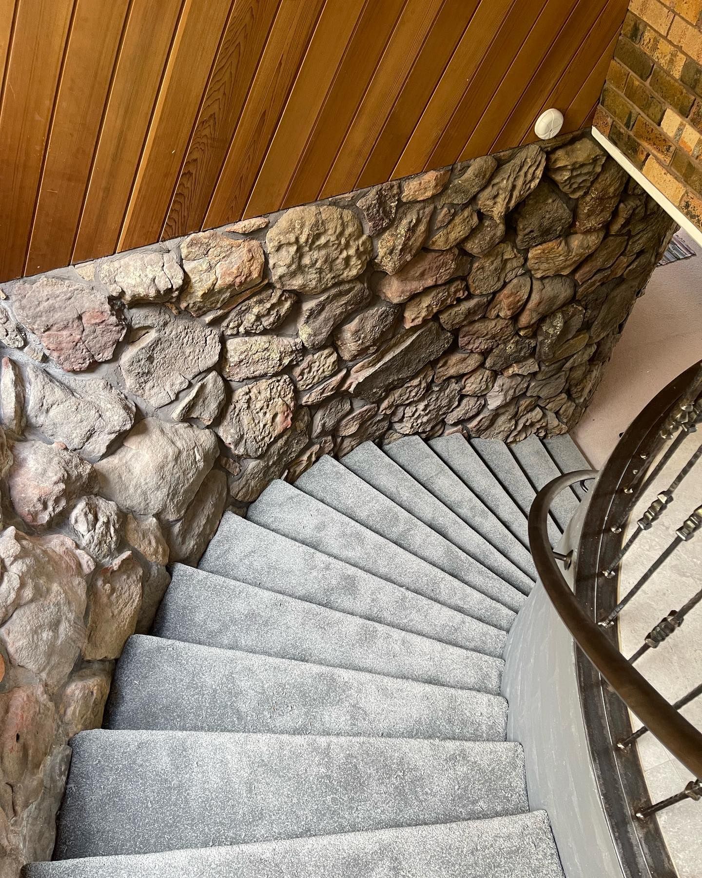 Curved stone staircase with gray steps, wood-paneled wall, and metal railing in a narrow interior space