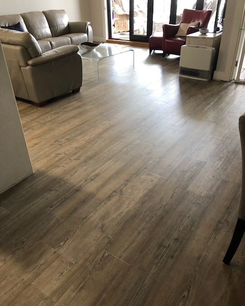 Modern living room with light wood flooring, beige sofas, and burgundy chairs near large windows