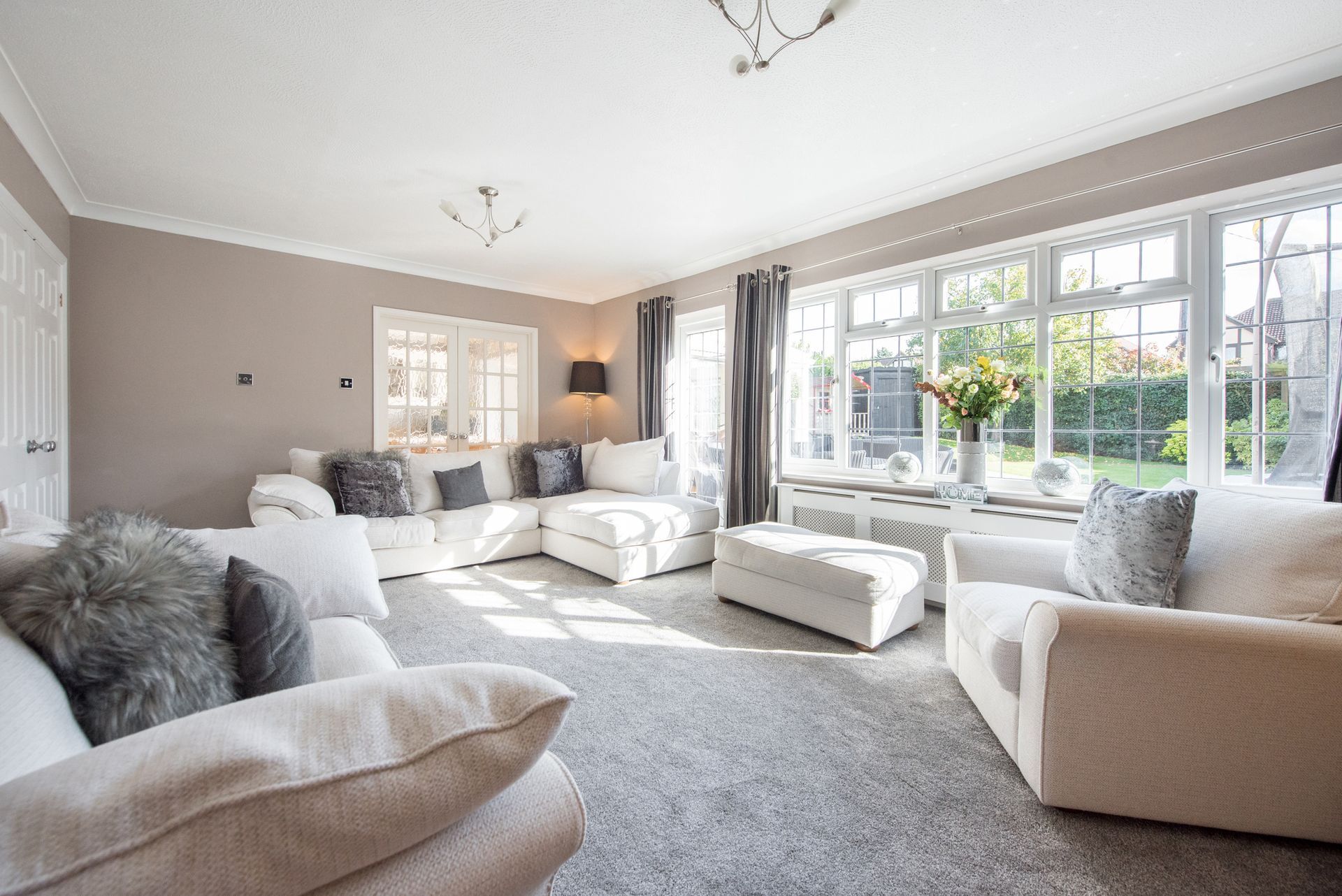 Bright living room with cream sofas, gray carpet, and large windows letting in natural light