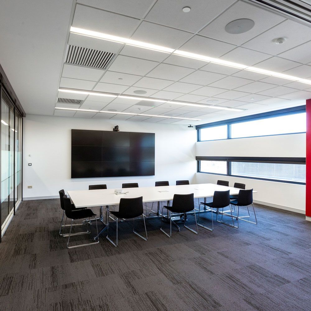 Modern conference room with white table, black chairs, large wall screen, and bright windows