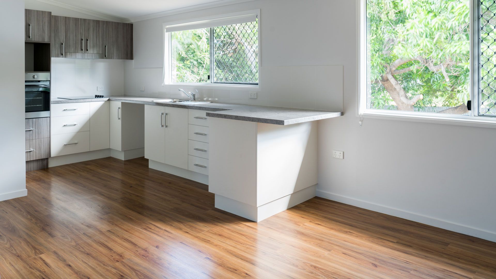 Bright modern kitchen with white cabinets, wood floors, and large windows letting in natural light