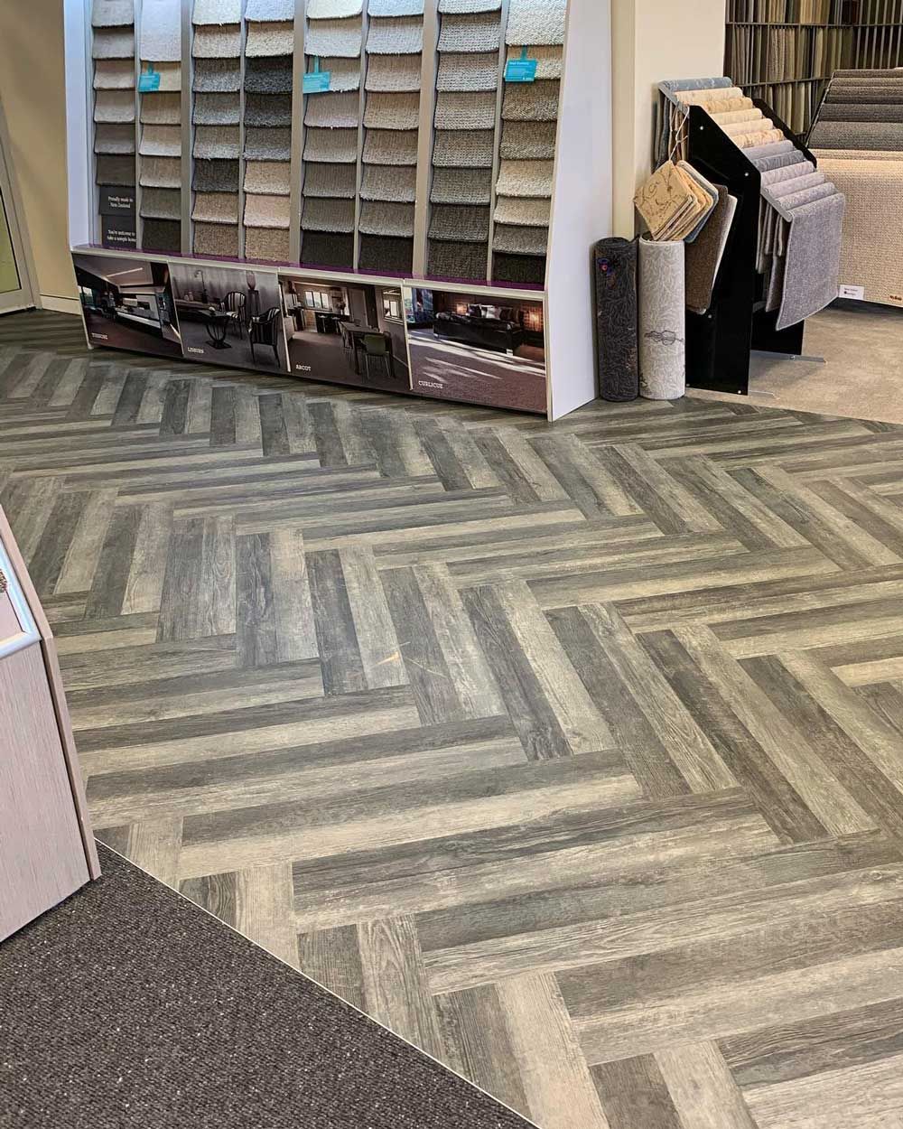 Carpet store display with patterned rugs, sample racks, and wall-to-wall carpet flooring