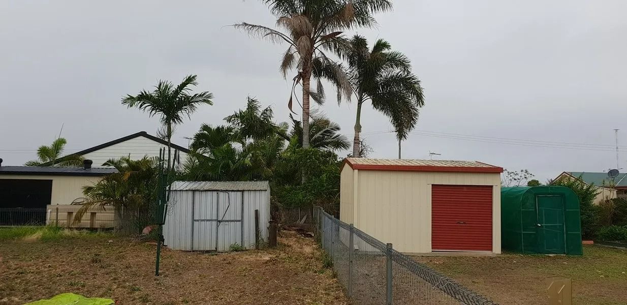 Rural Yard With Small Sheds, a Palm Tree, and a Red Garage Door — Barlows Tree Services in Rockhampton, QLD