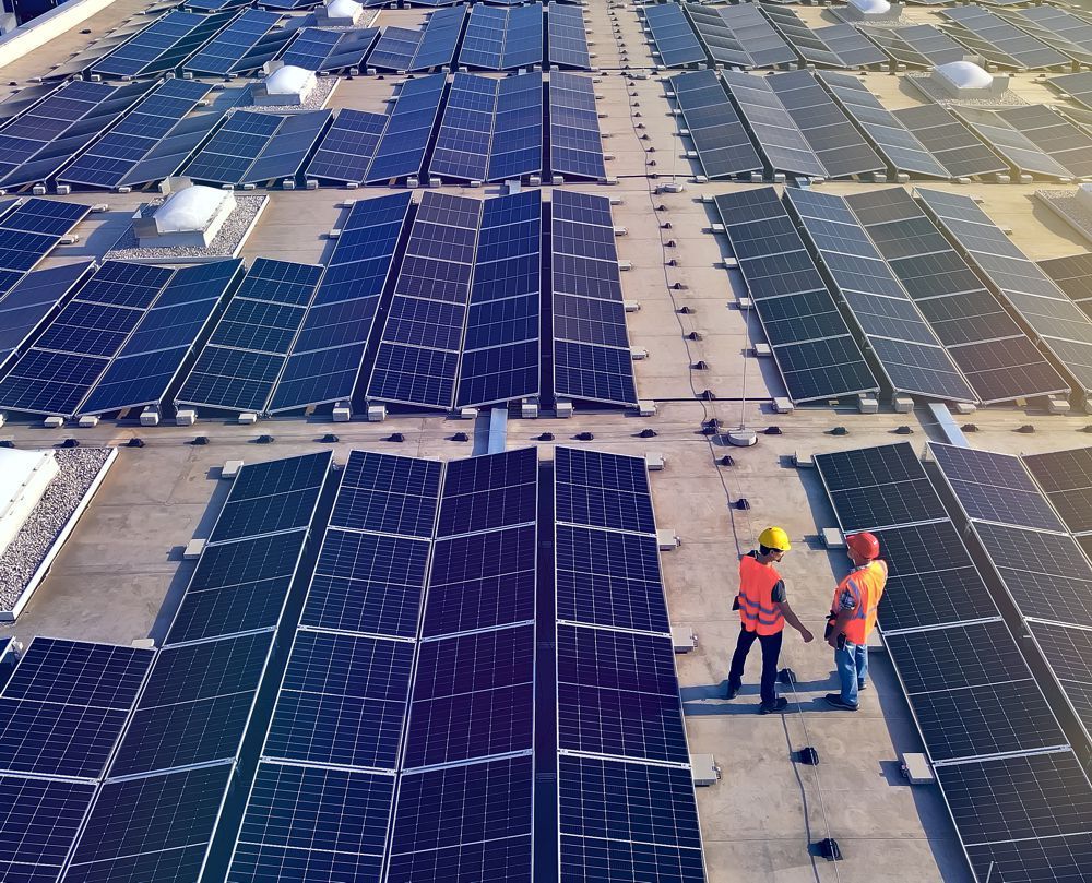 Workers in hard hats inspecting solar panels on a rooftop.