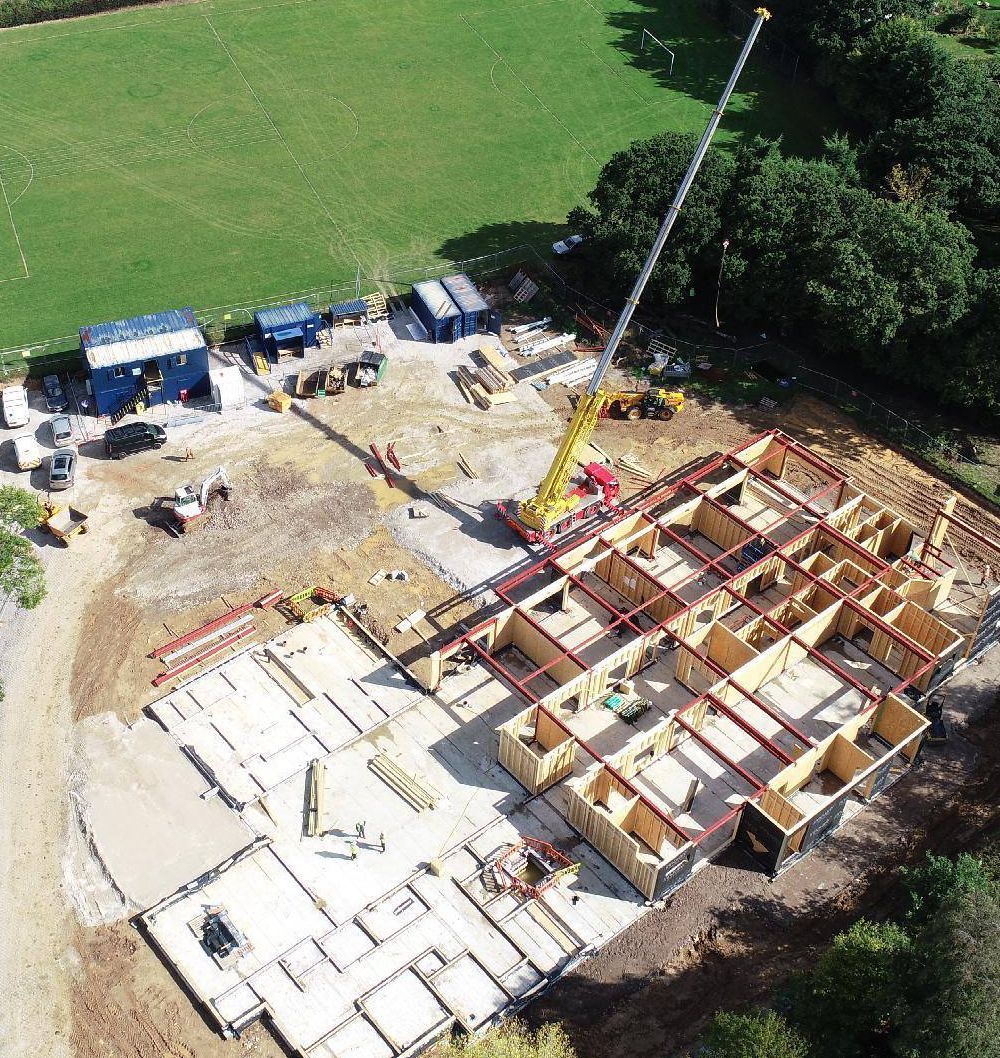 Construction site with a partially built wooden frame structure, crane, and equipment.