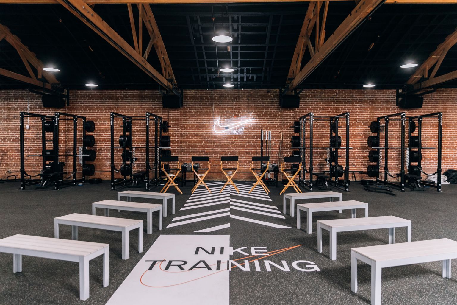 Gym interior with white benches arranged in a semi-circle facing five director chairs and a Nike Training floor logo.