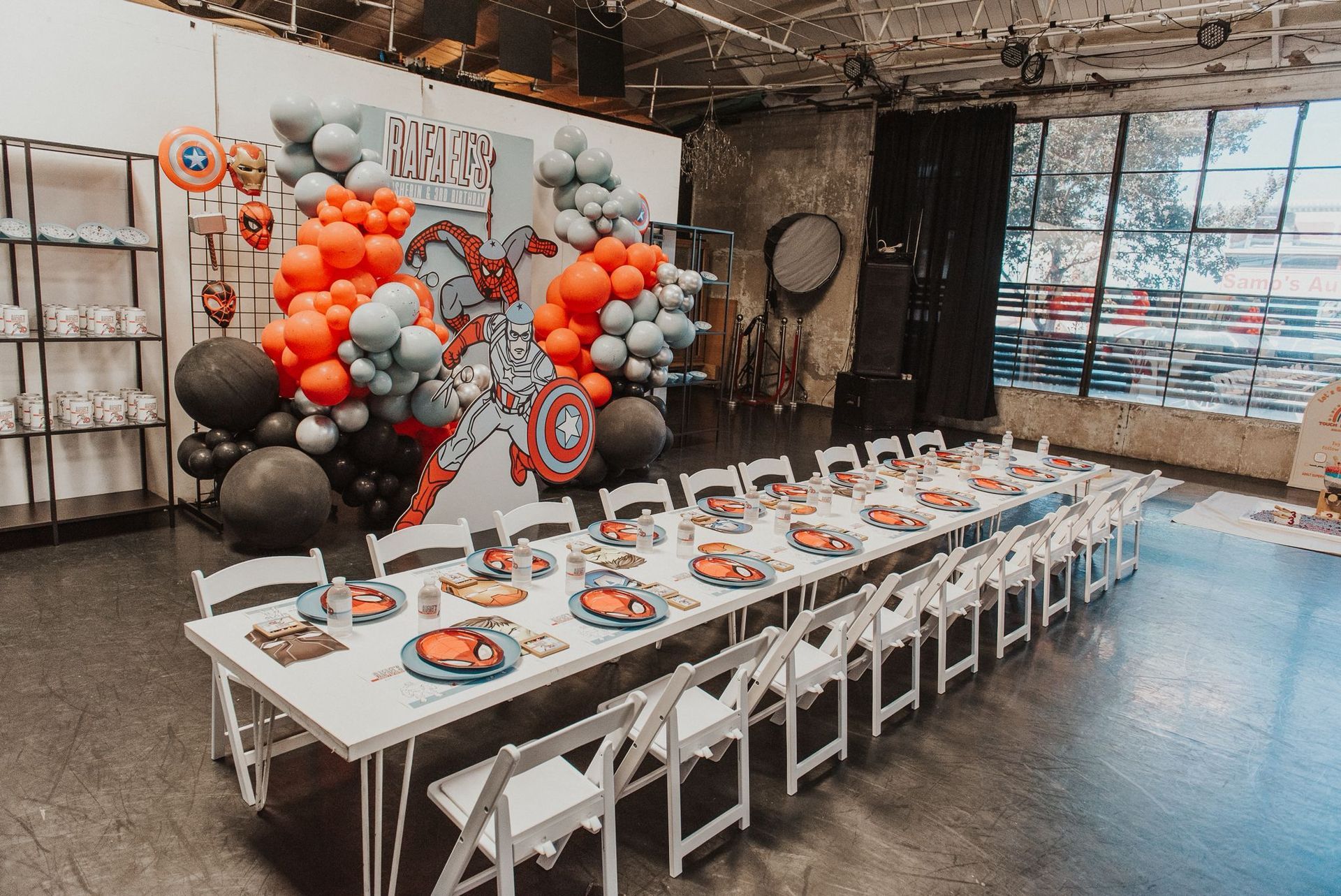 A long table set for a superhero-themed party, featuring balloon arches, character decorations, and place settings.