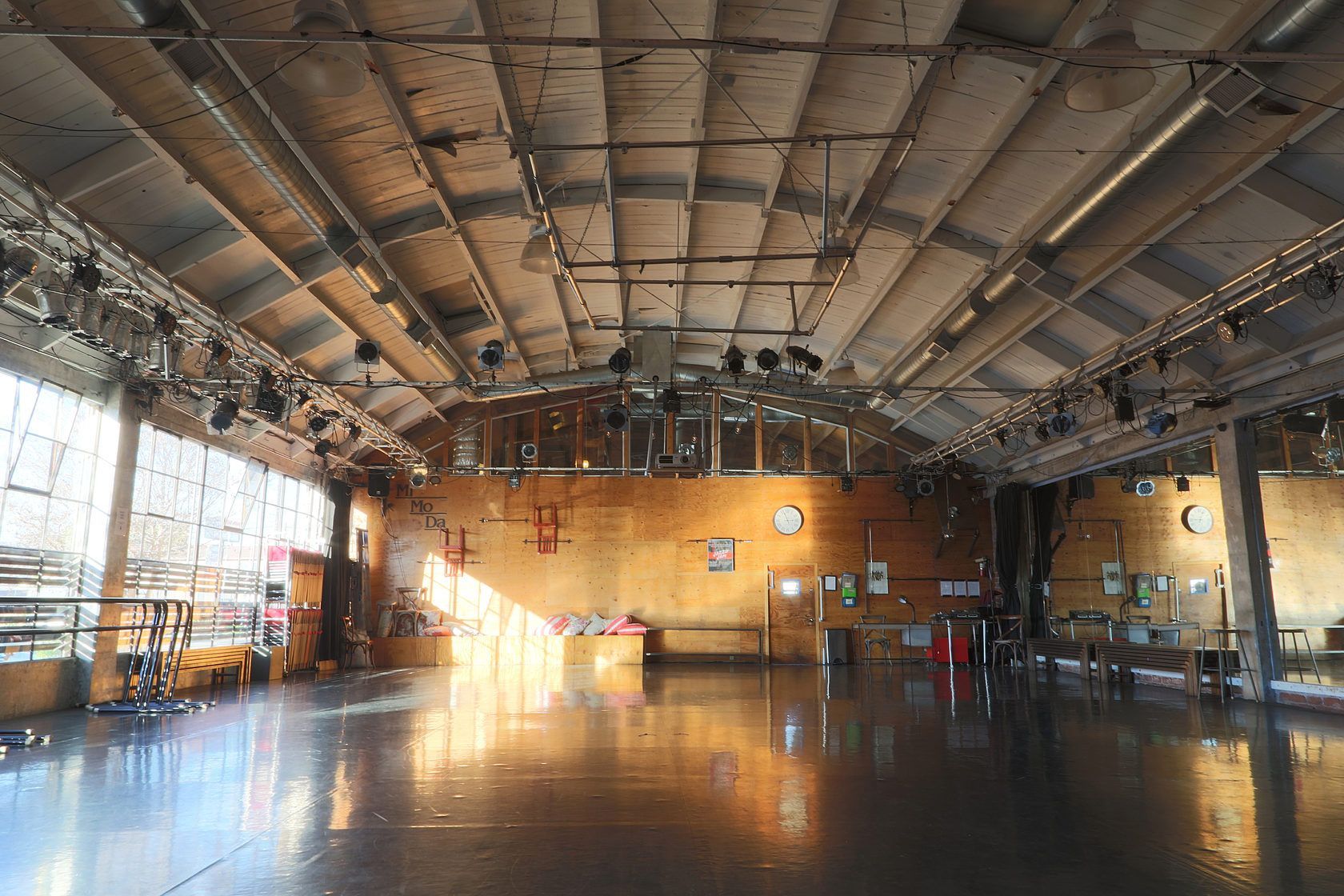 Large, empty industrial-style room with a high, vaulted ceiling, light-colored wooden walls, and a glossy floor.