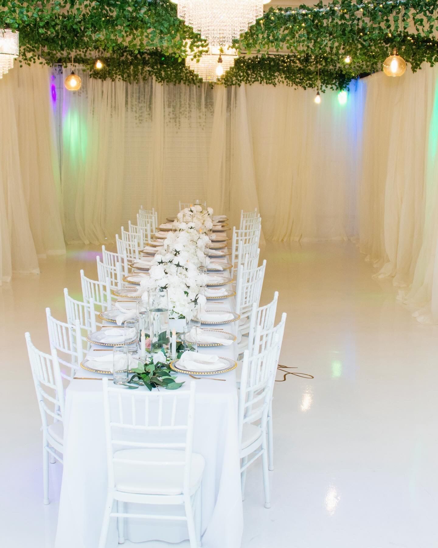 A long white table and chairs in a room with a chandelier hanging from the ceiling.