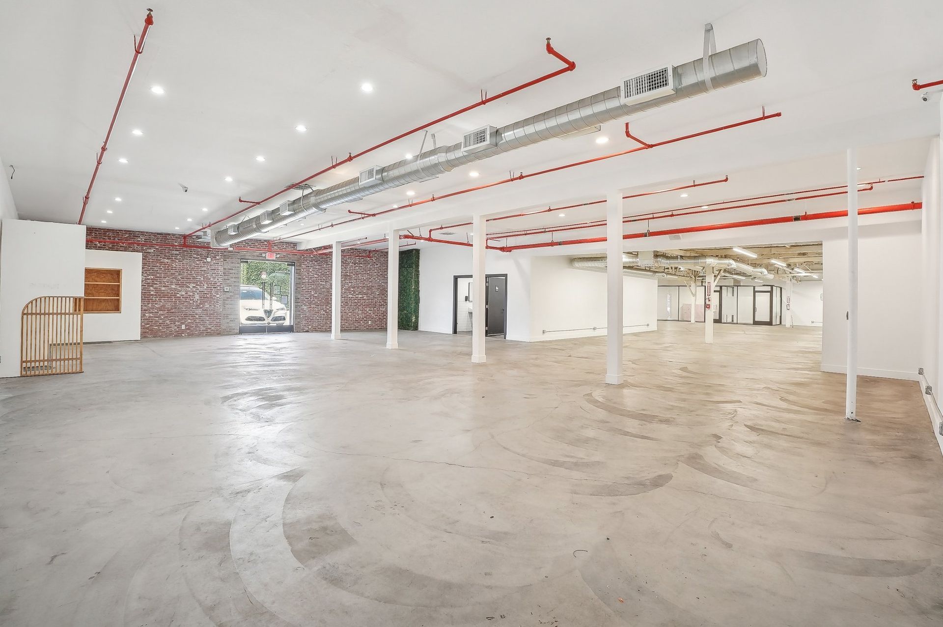 An empty, spacious commercial room with white walls, a polished concrete floor, exposed brick, and industrial ceilings.