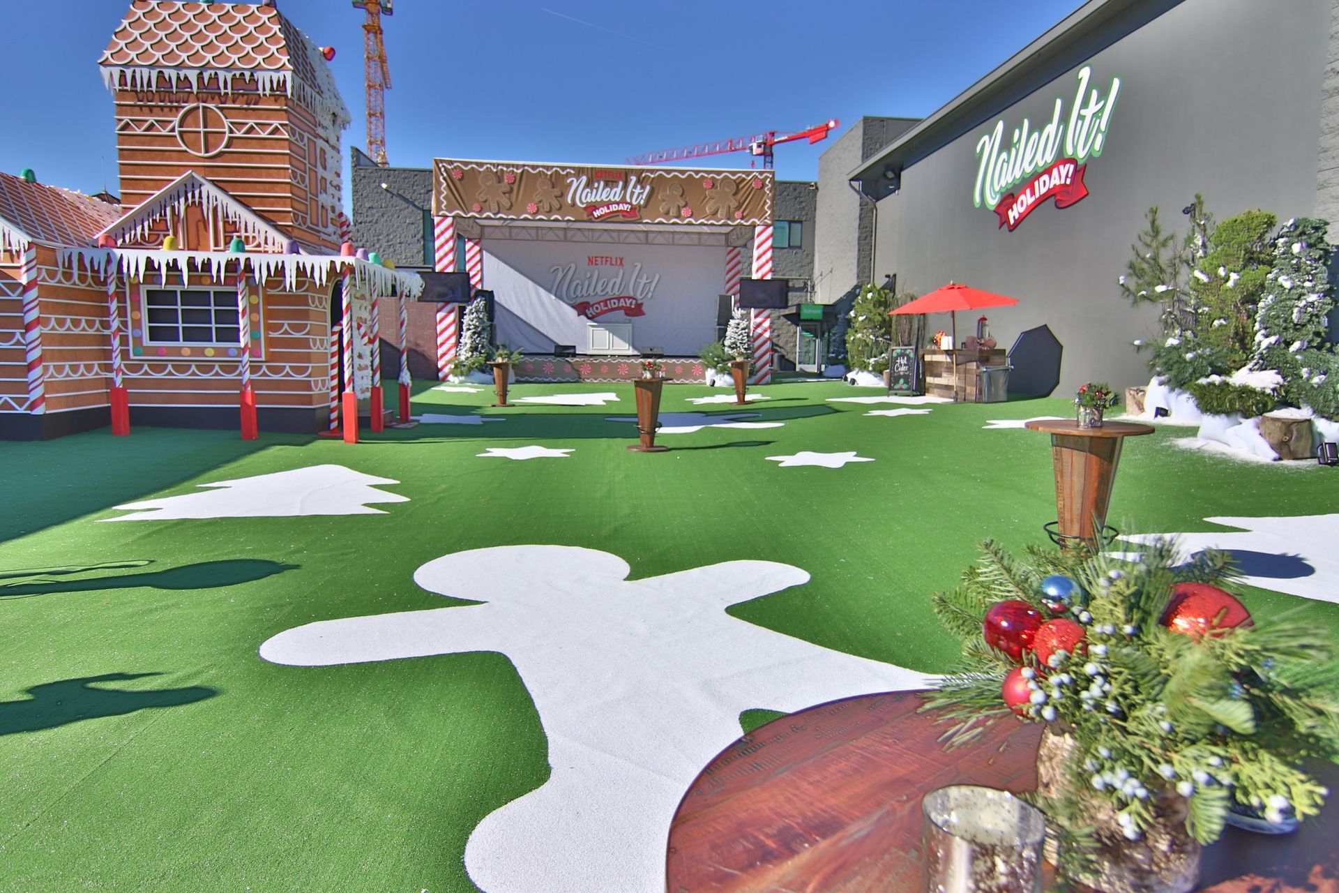 An outdoor venue decorated for Christmas with a gingerbread house, a stage, and white gingerbread-shaped floor decals.