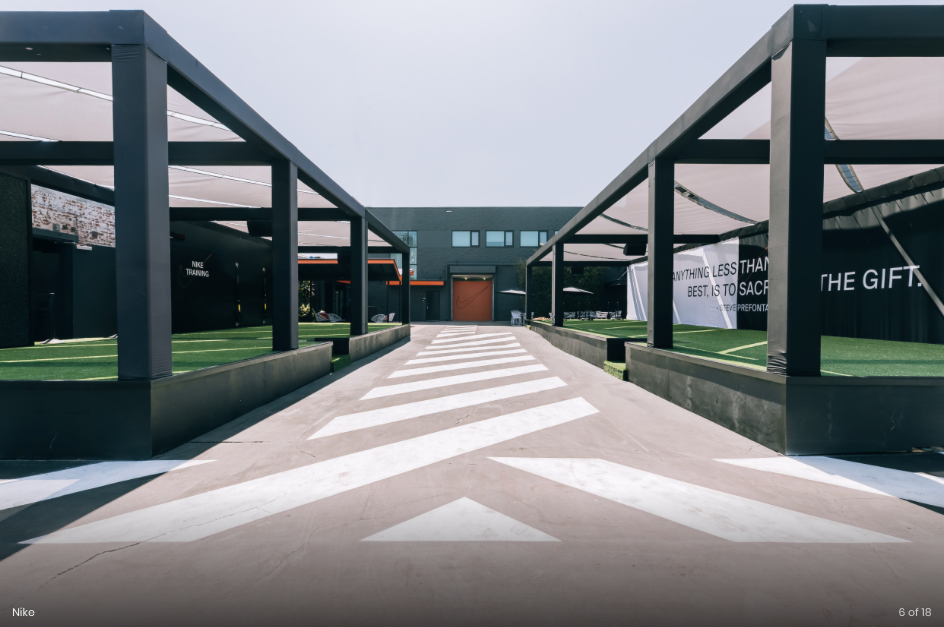 A central pathway with white stripes leads to a building flanked by two symmetrical black modern structures with awnings.