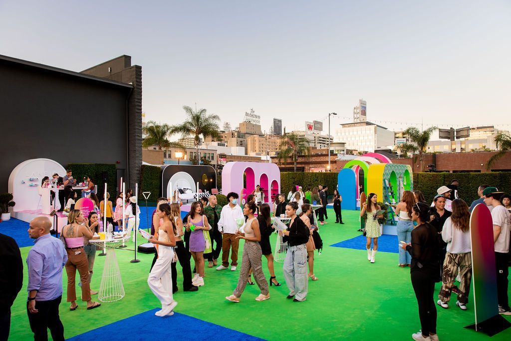 People gather on a green rooftop with bright, colorful arch structures against a city skyline at dusk.