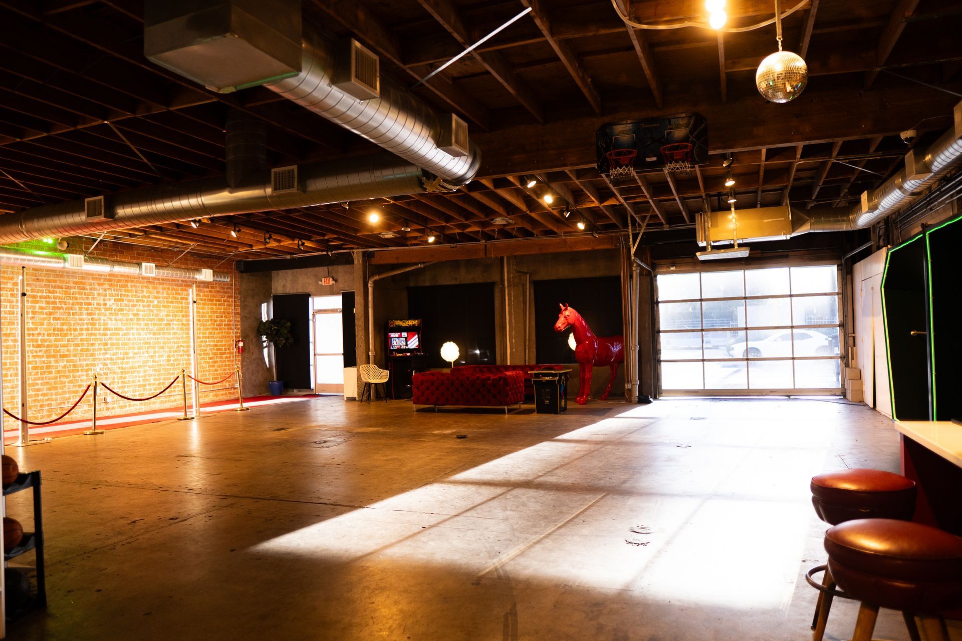 An open, industrial event space with high ceilings, exposed ductwork, brick walls, and a large red horse sculpture.