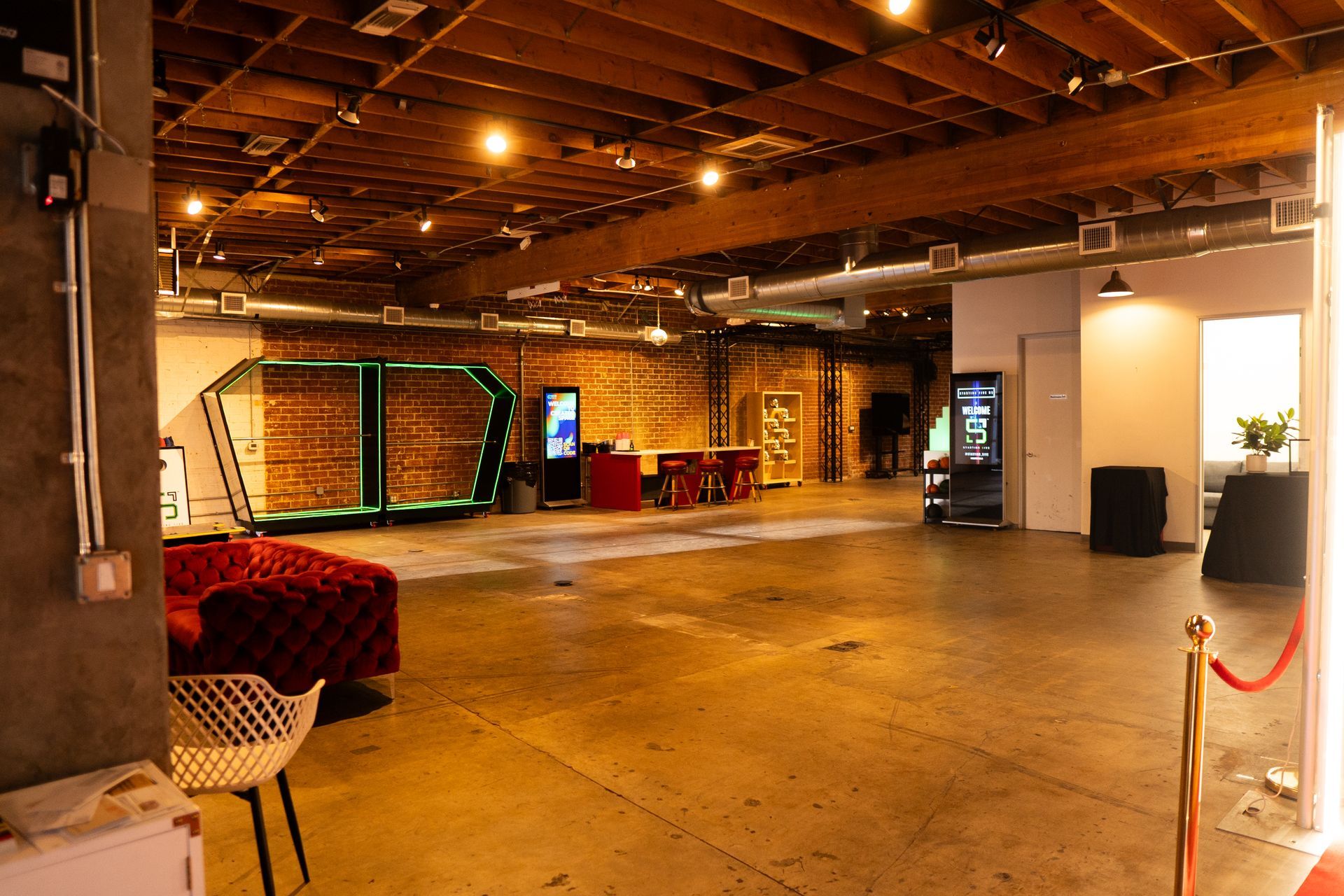 A spacious, industrial-style room with a red sofa, exposed brick walls, wooden ceiling beams, and decorative lighting.