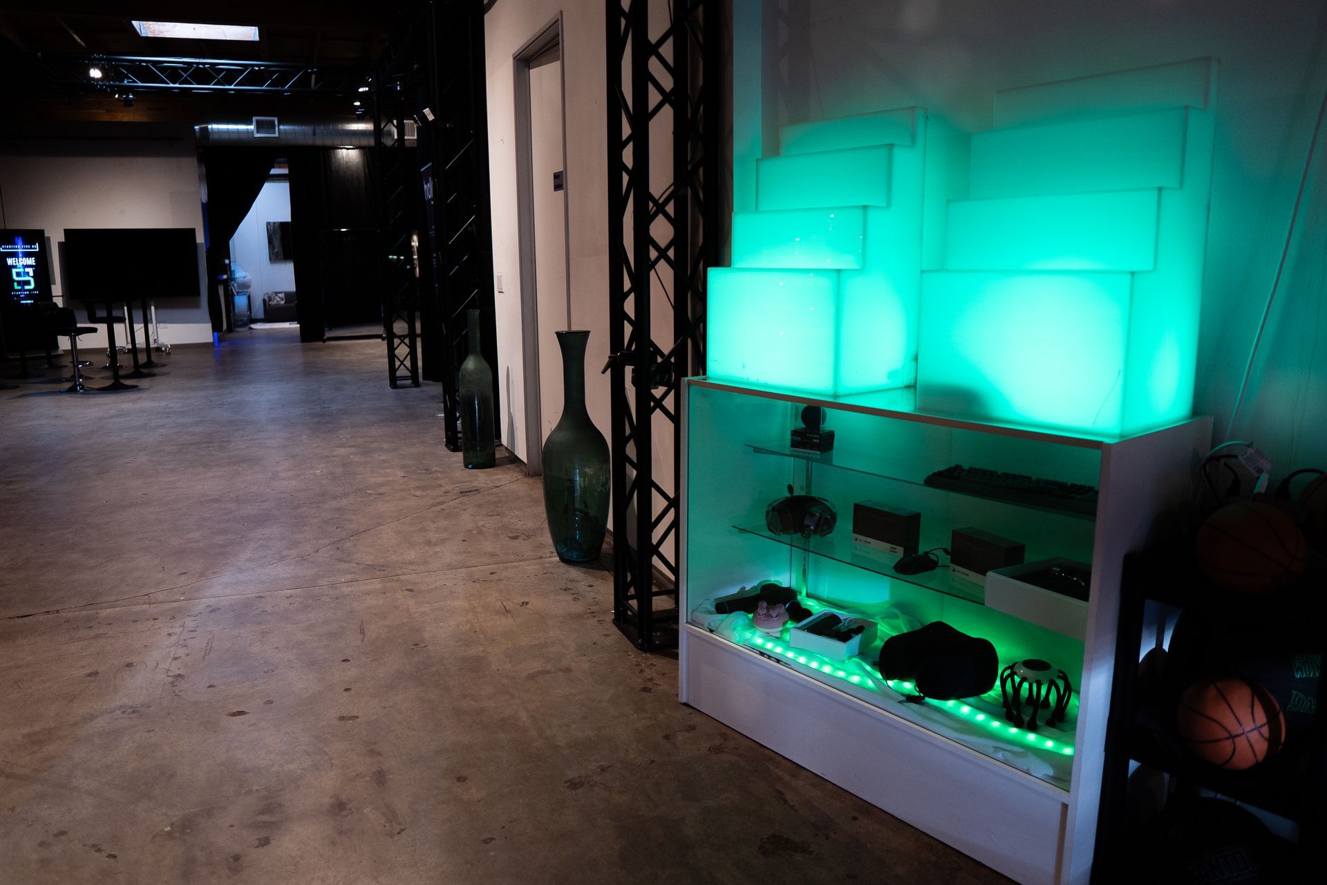 A display case with glowing green blocks on top sits in a room with concrete floors, leading to a dark hallway.
