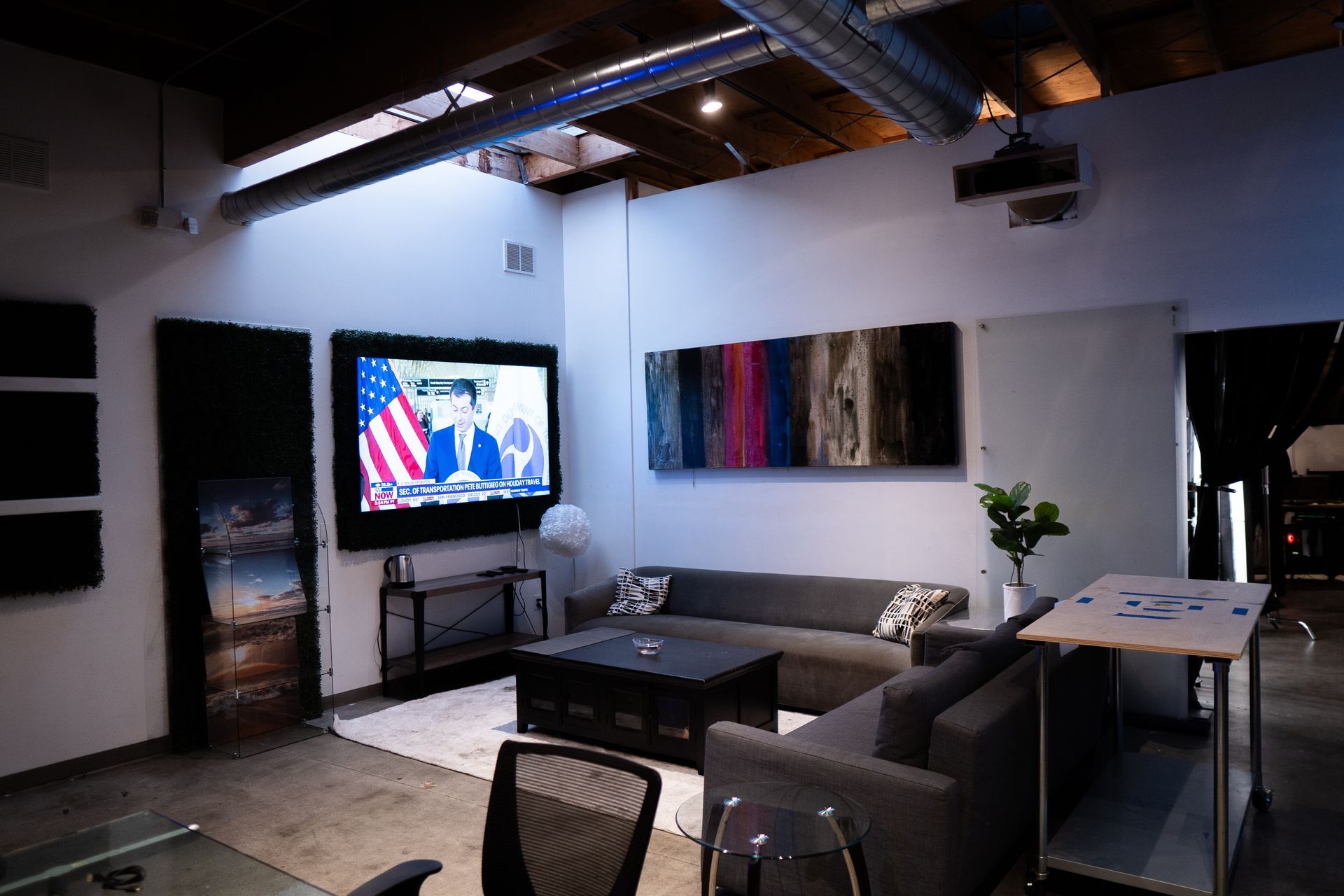 A modern lounge area with two gray sofas, a coffee table, a large wall-mounted TV showing news, and textured wall art.
