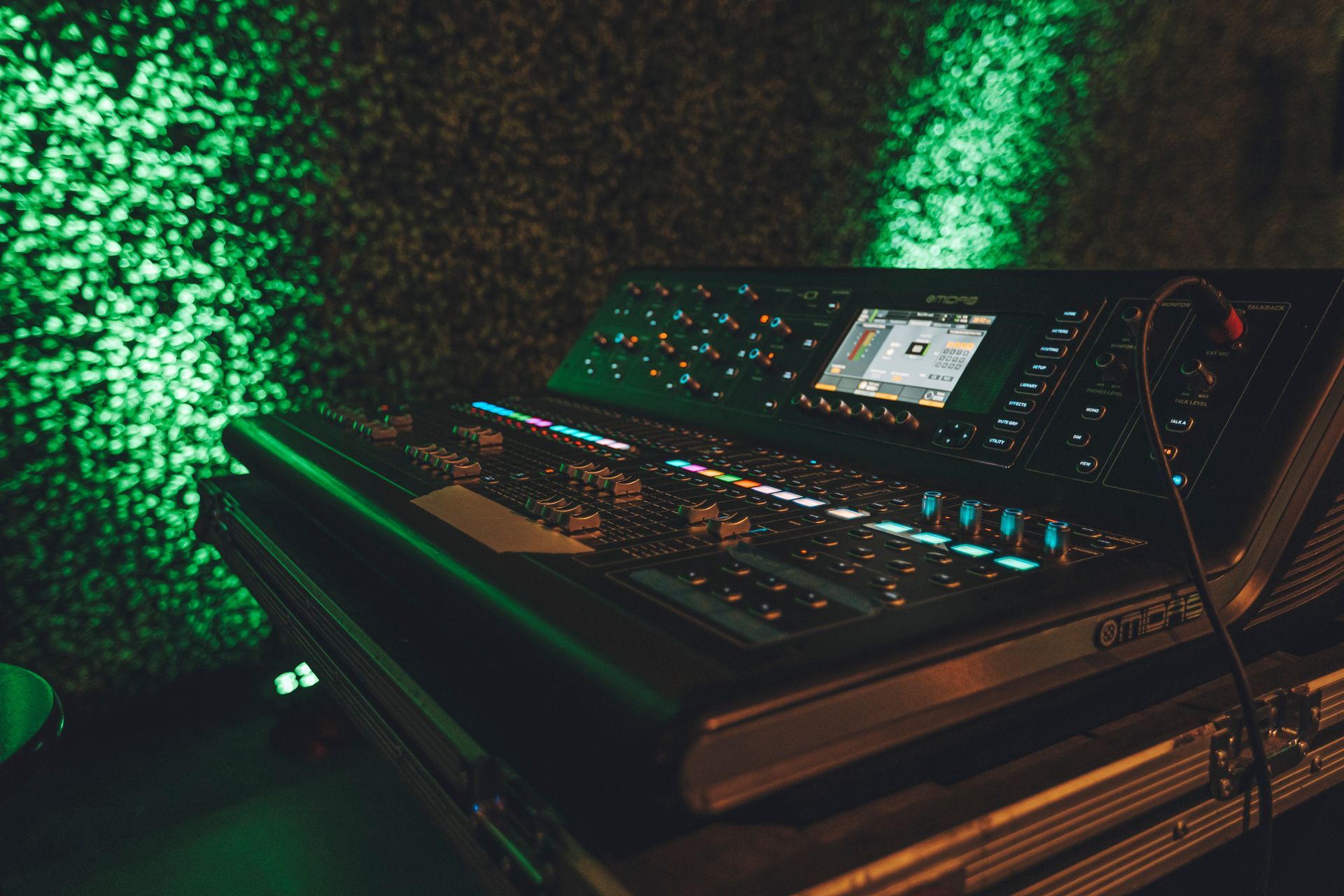A mixer is sitting on top of a case in a dark room with green lights behind it.