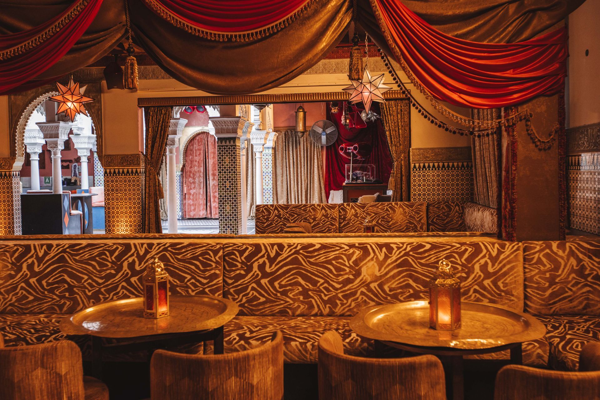 A restaurant with tables and chairs and a red curtain hanging from the ceiling.