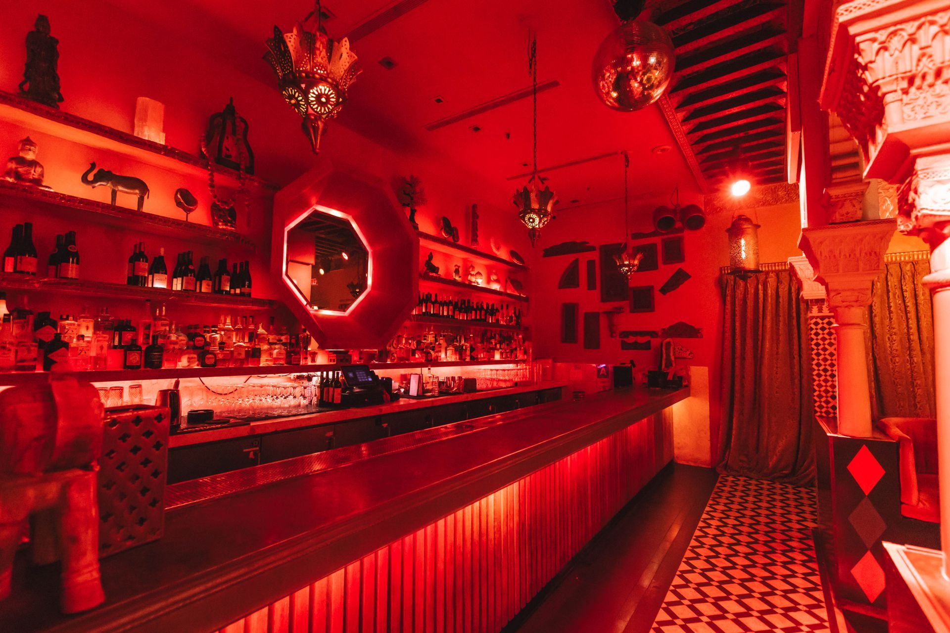 A long red bar in a dark room with a mirror on the wall.