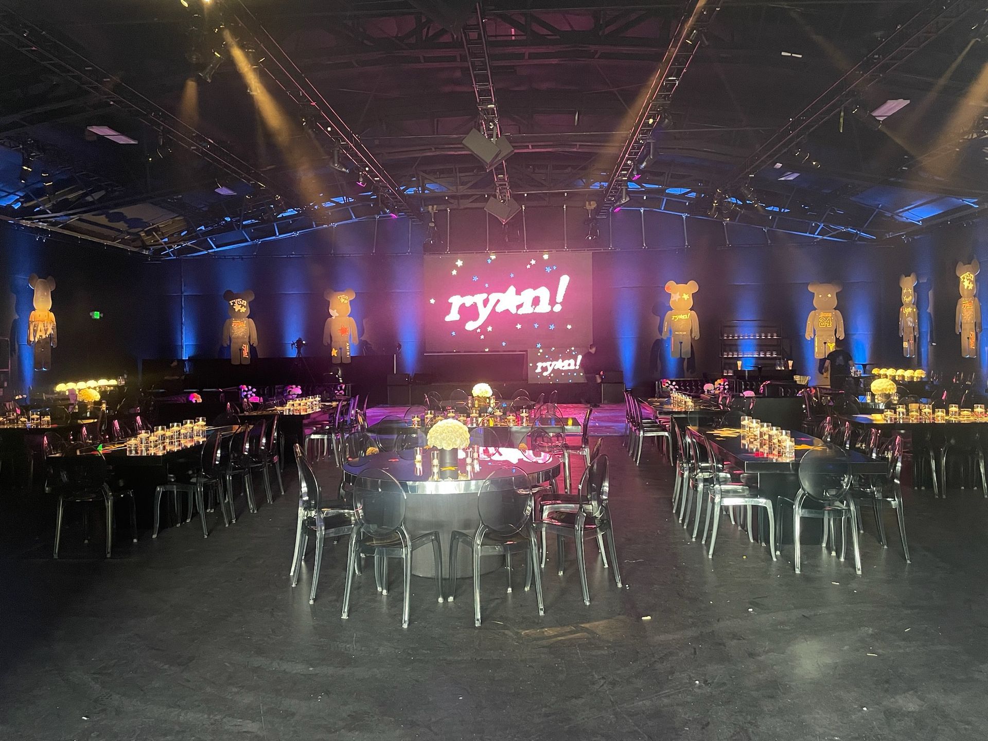 A dark, event-lit room features tables and chairs arranged for a party, with 