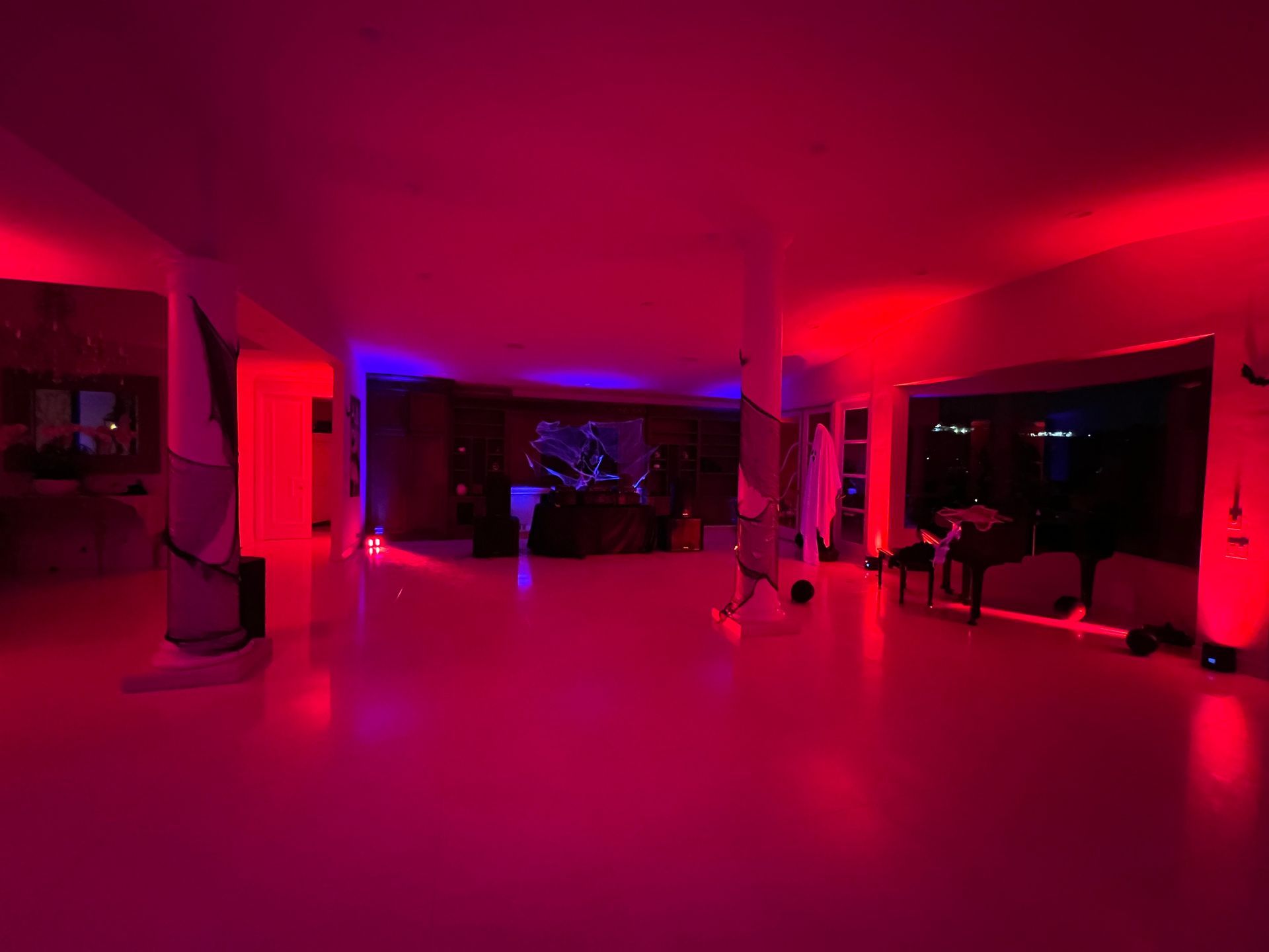 A spacious interior room at night lit by vibrant red and purple neon lights, featuring structural columns and furniture.