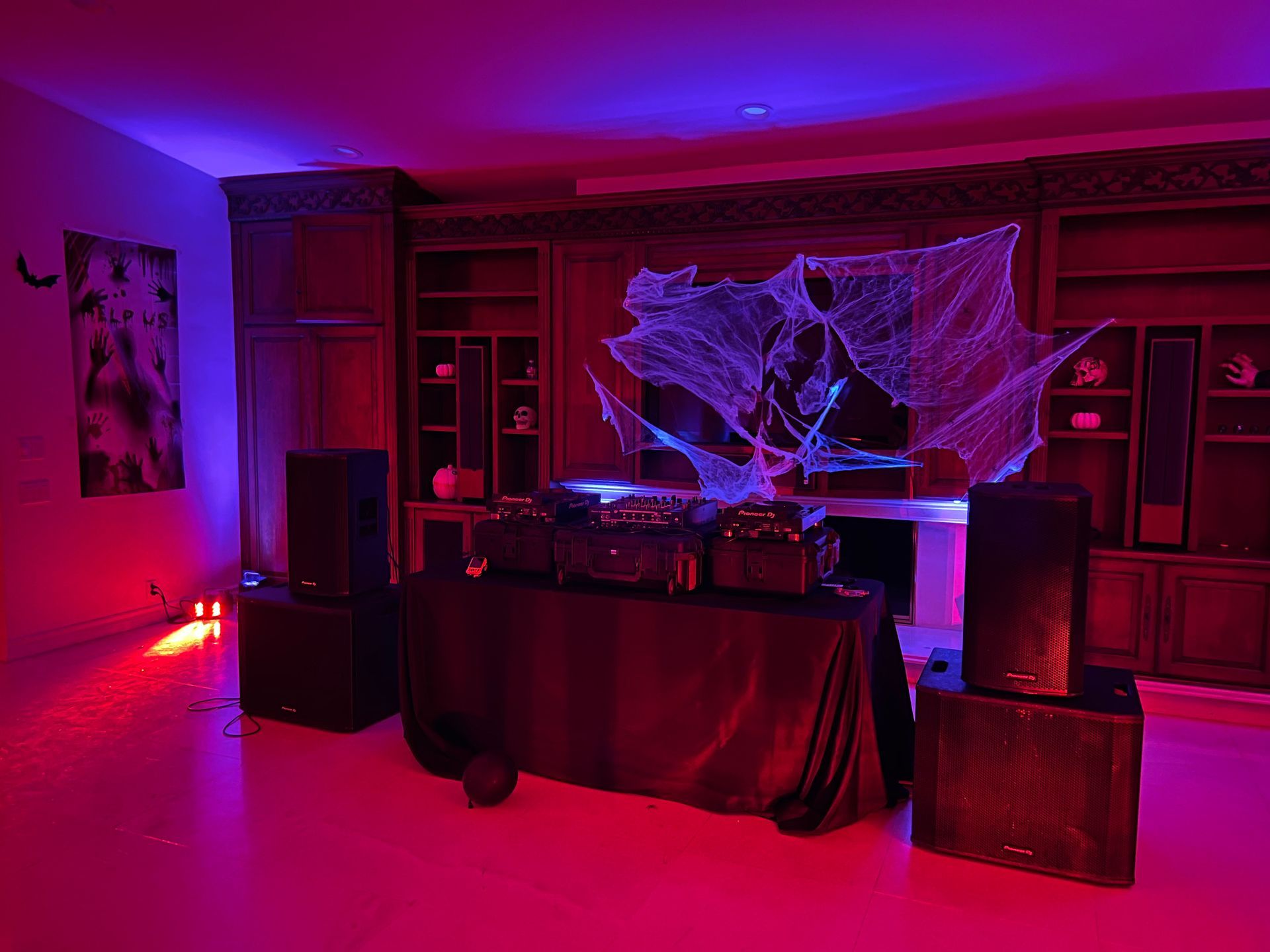 A room decorated for Halloween with a DJ setup, covered in cobwebs and bathed in red and purple lighting.