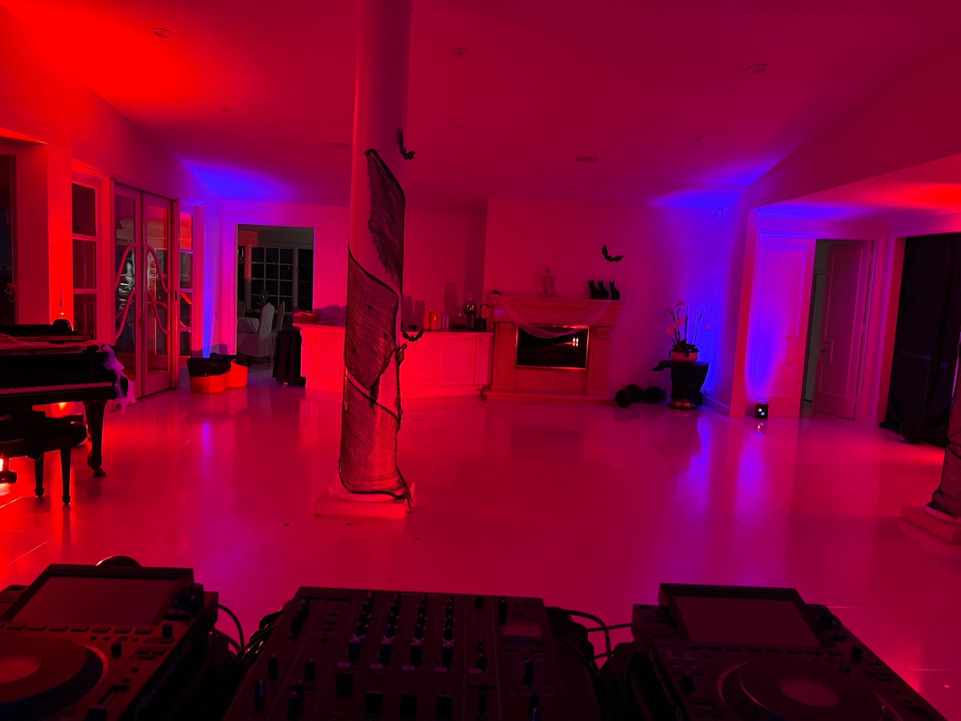 A DJ controller sits in the foreground overlooking a large, empty room lit by vibrant red and blue neon lighting.