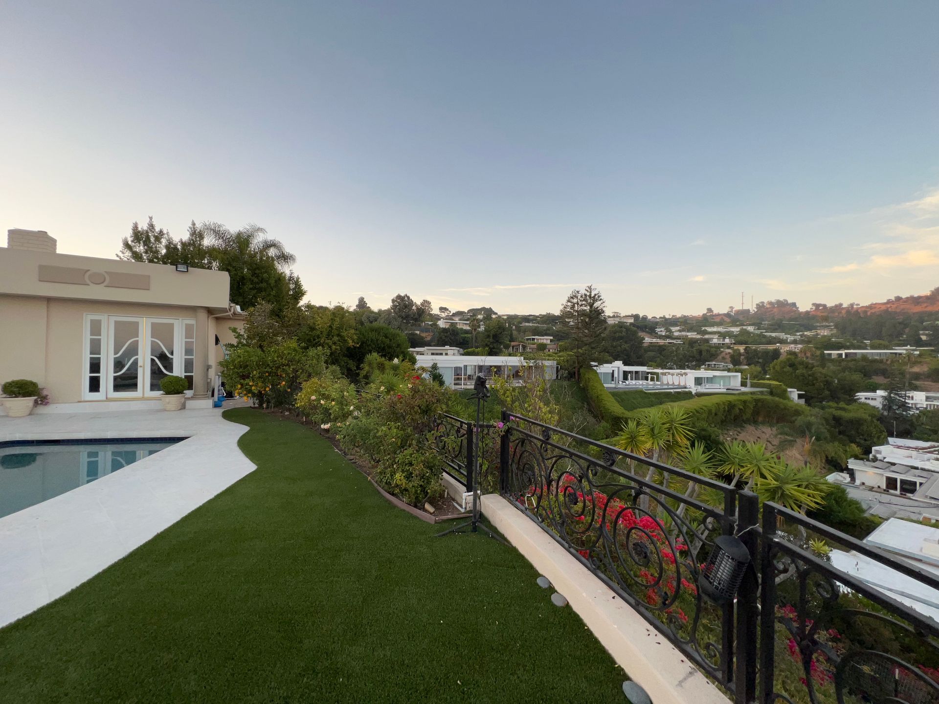 A scenic view from a patio with a swimming pool and lawn, overlooking a hillside residential area at dusk.