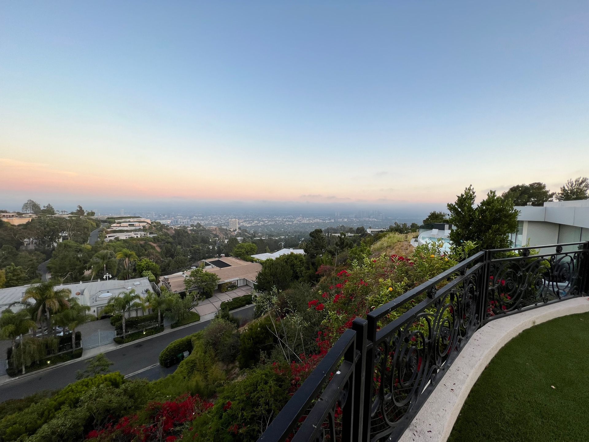 A high-angle view overlooking a lush hillside neighborhood toward a hazy ocean horizon at sunset.