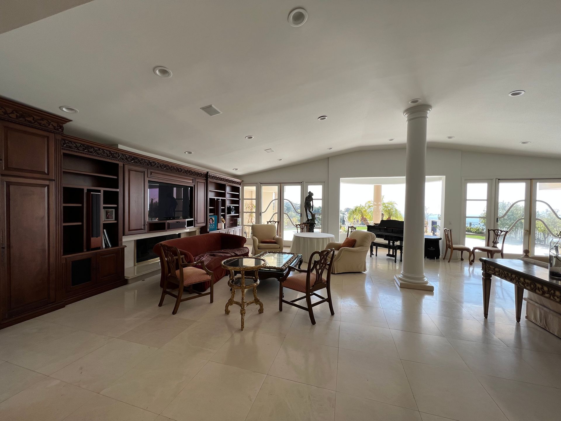 Spacious living room with tile floors, large built-in shelves, a seating area with red sofa, and a piano near glass doors.