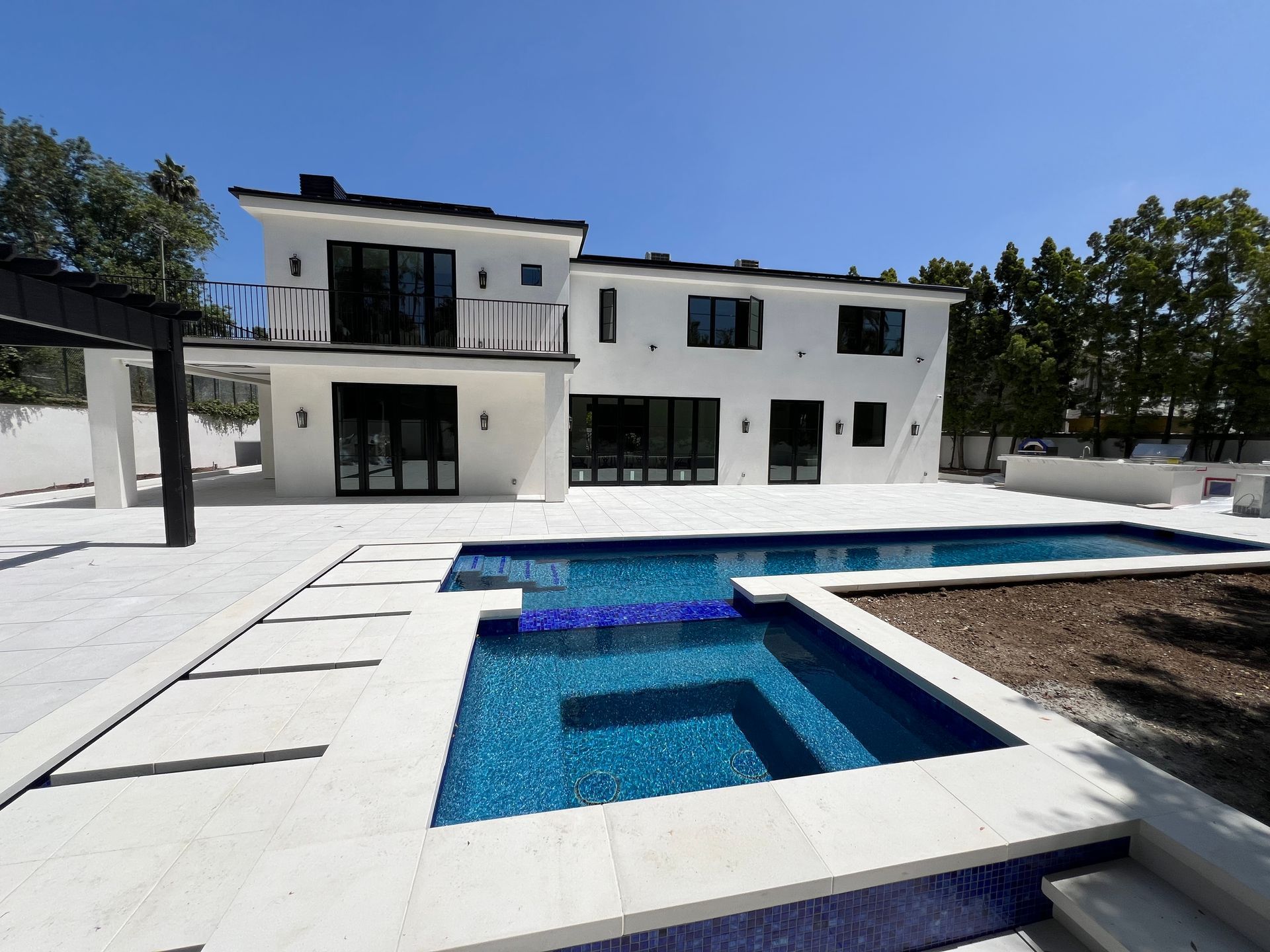 A modern white two-story house with a backyard pool and spa, set against a clear blue sky.