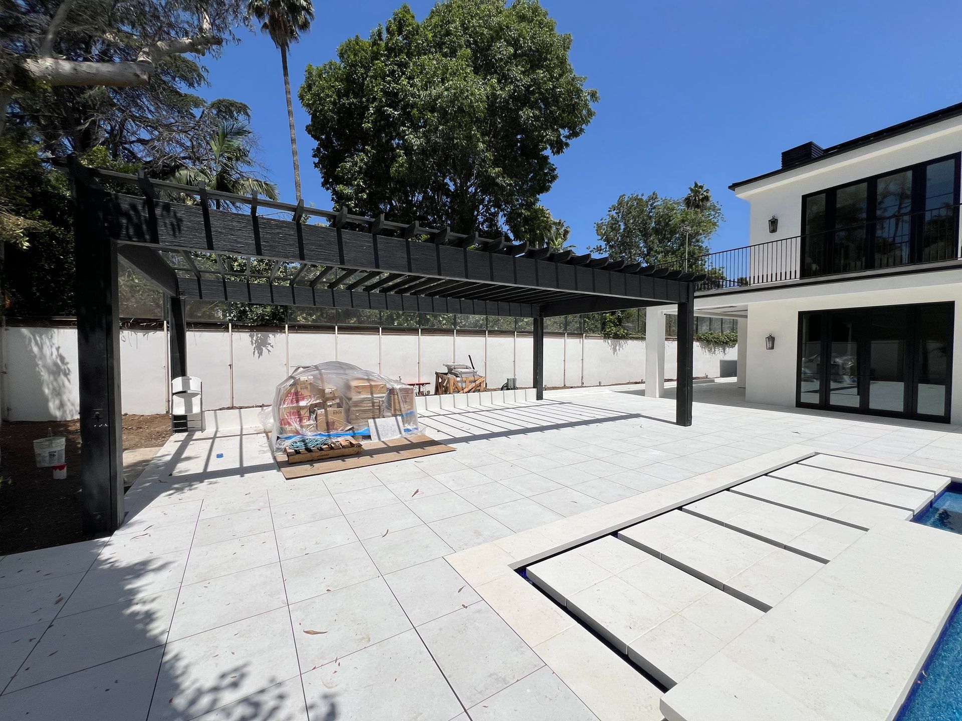 A modern backyard featuring a white patio, a black pergola, and a swimming pool with a black automatic cover.