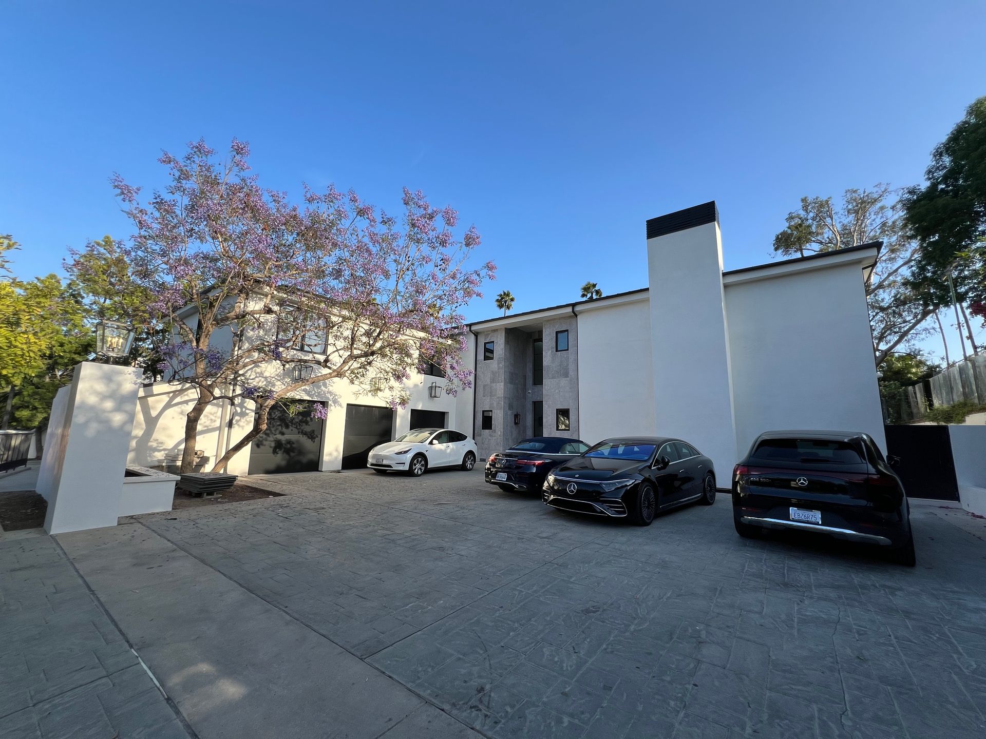 A multi-story white apartment building with a gray concrete parking lot and several parked cars under a blue sky.