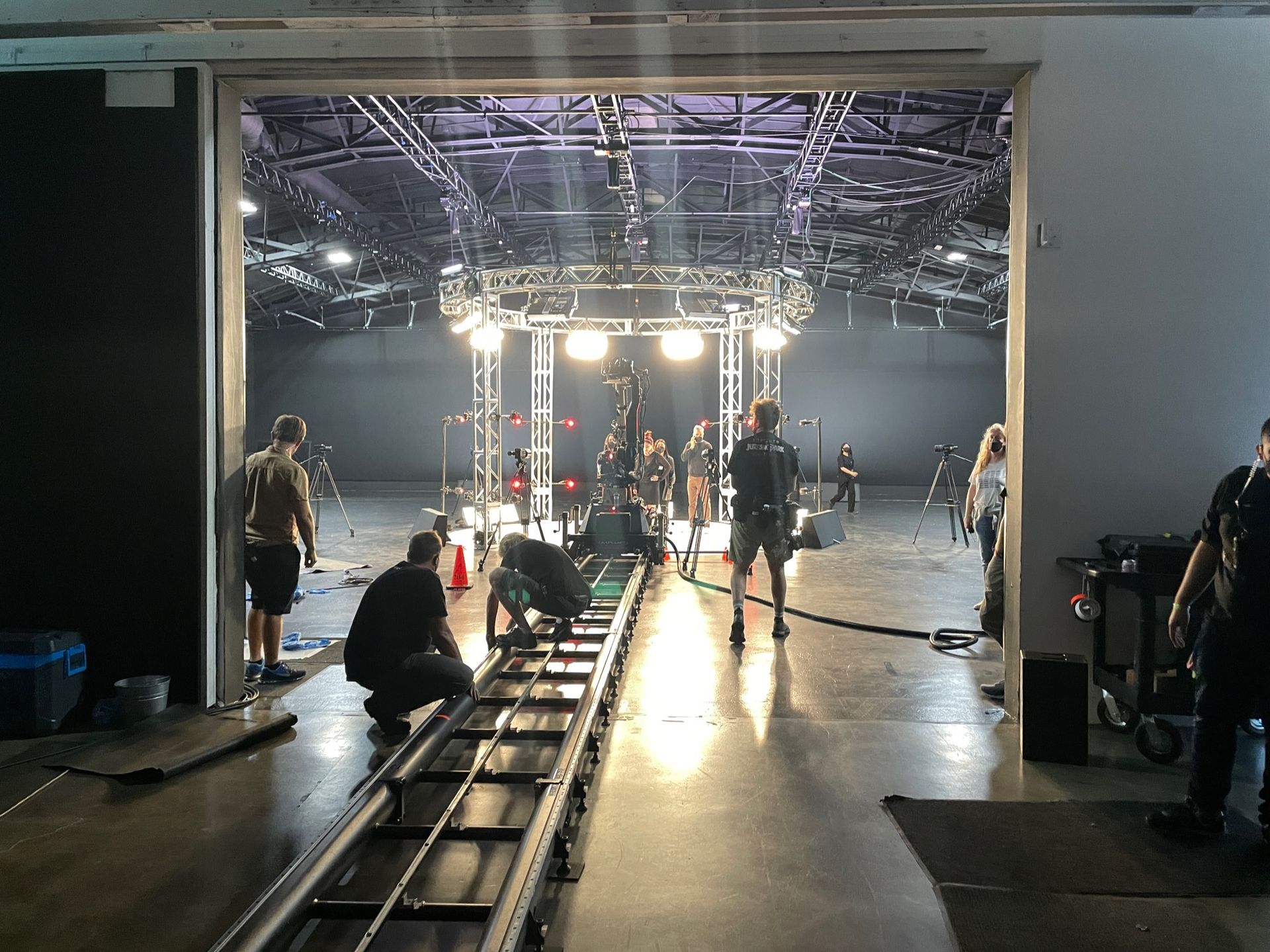 A crew sets up lighting and camera tracks on a film studio soundstage.