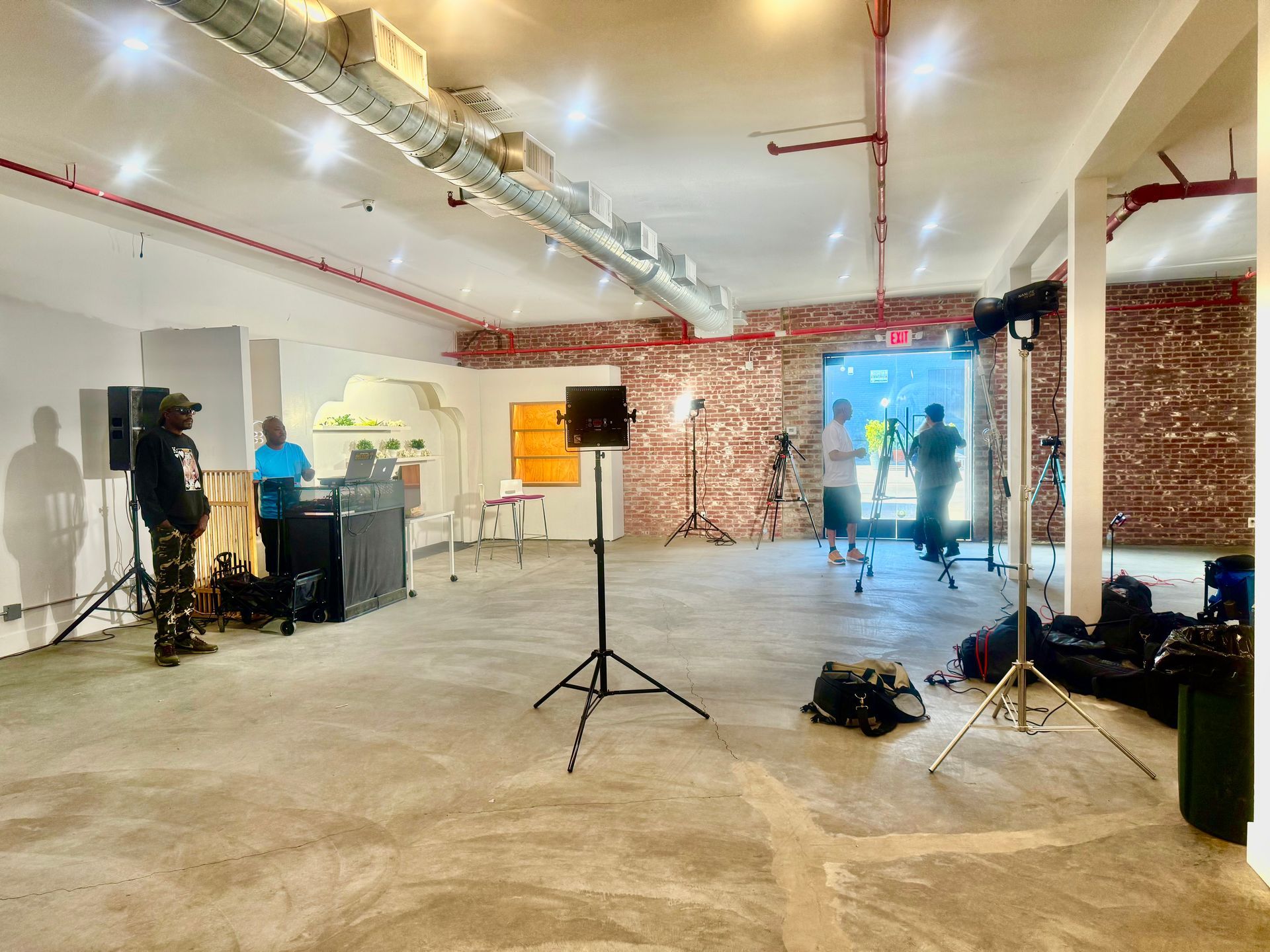 A sparsely furnished room with industrial architecture, photography equipment, and people standing in the background.