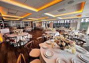 A banquet hall set for a wedding reception with round tables featuring white tablecloths, floral centerpieces, and chairs.