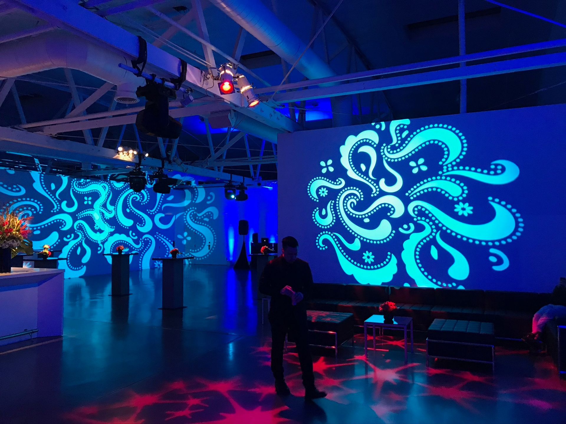 A room bathed in blue light features walls with glowing teal patterns and a person standing in the center.