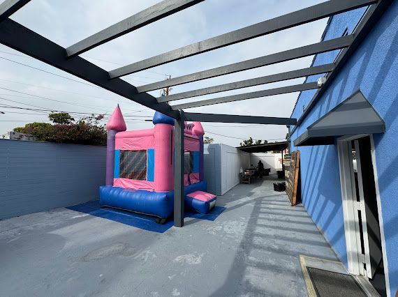 A pink bouncy castle is sitting under a canopy in front of a blue building.