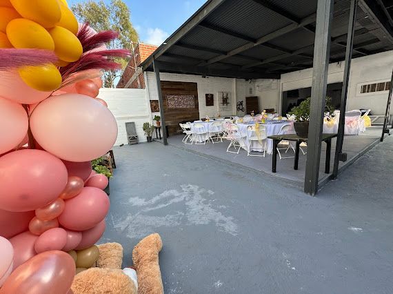 A teddy bear is sitting on the ground next to a bunch of balloons.