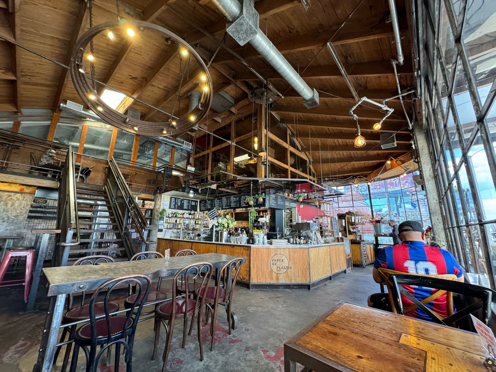 Rustic, industrial-style café interior with a wooden ceiling, exposed beams, round pendant lights, and bar seating.