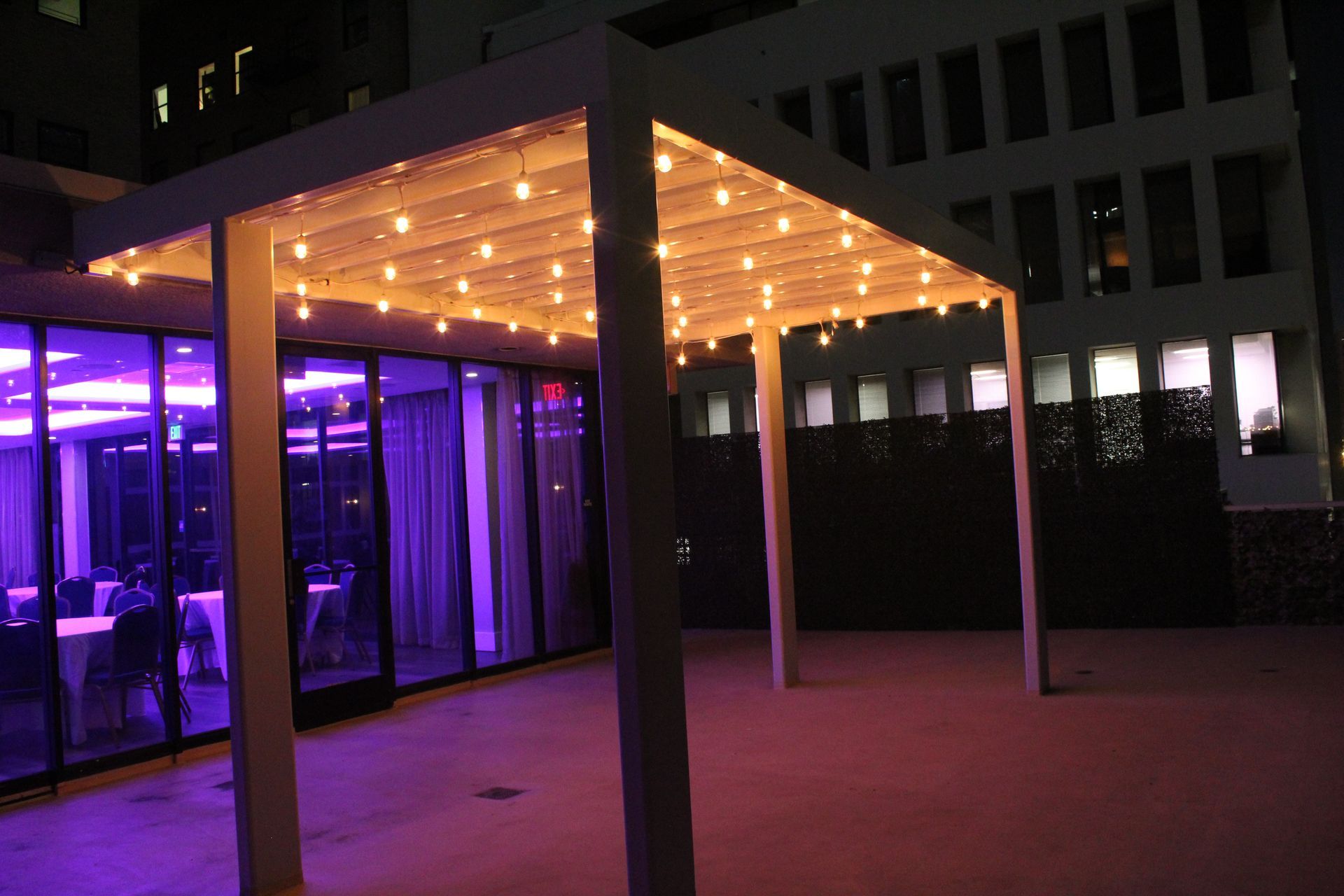 A covered area with purple lights and a building in the background