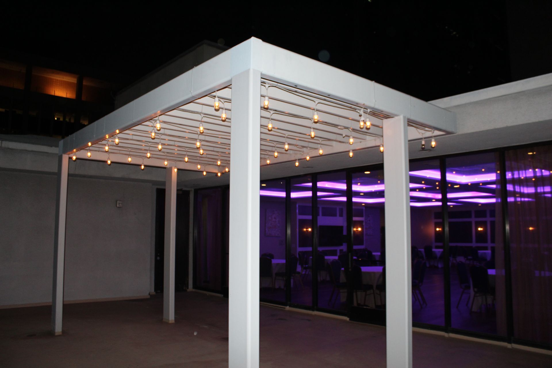 A white pergola with lights hanging from it is lit up at night.