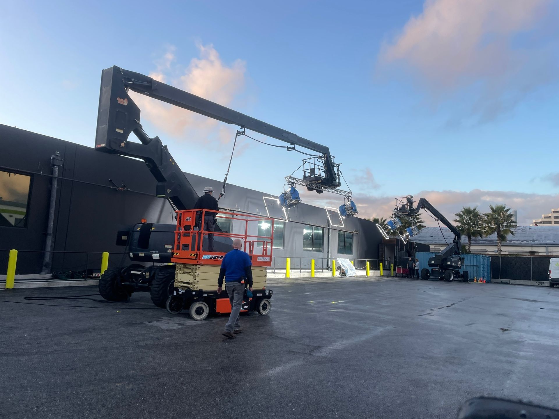 Workers operate boom lifts and a scissor lift to perform maintenance on a dark-colored building exterior.