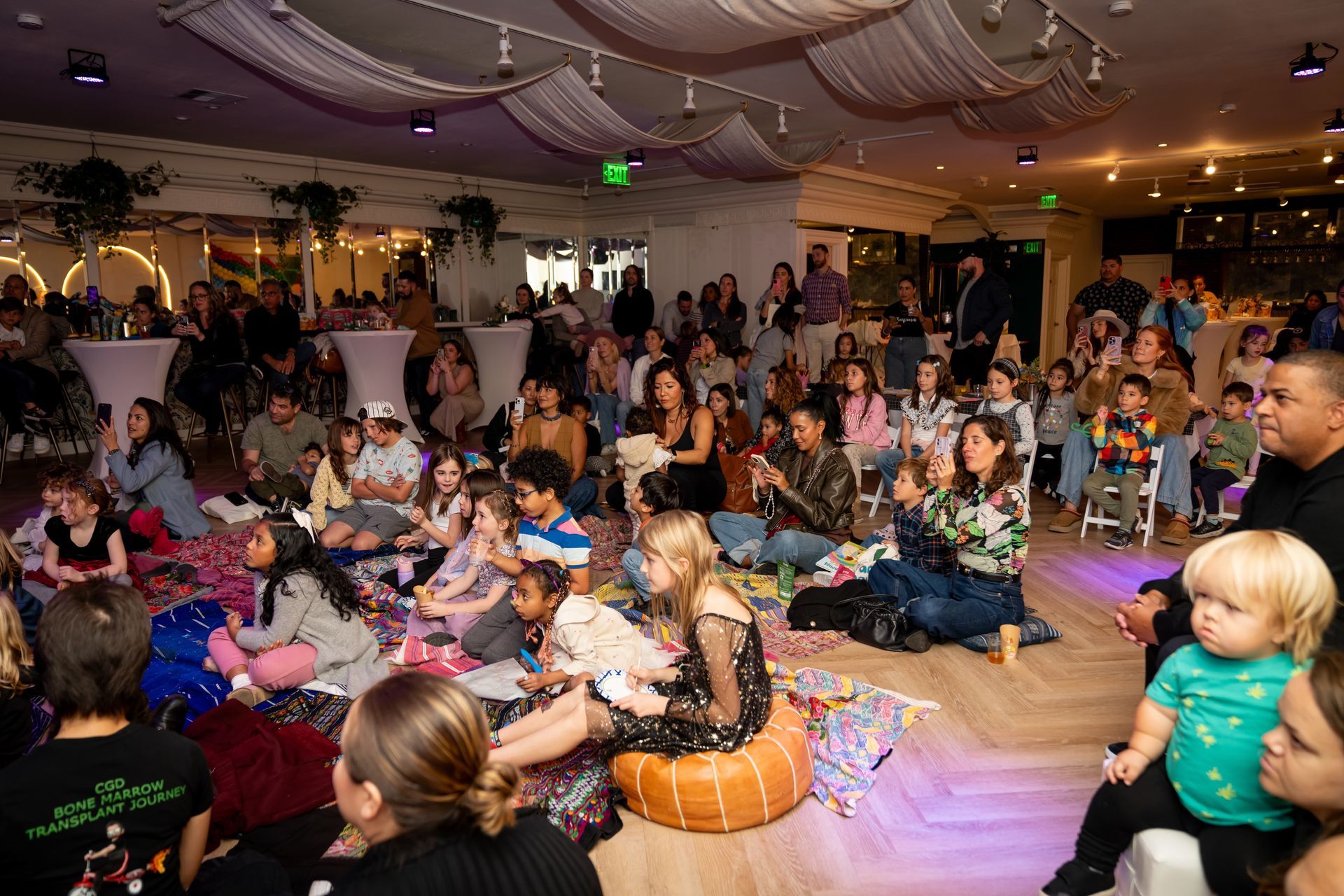 Crowded dance floor at a party, with people seated on the floor watching and a toddler in the foreground