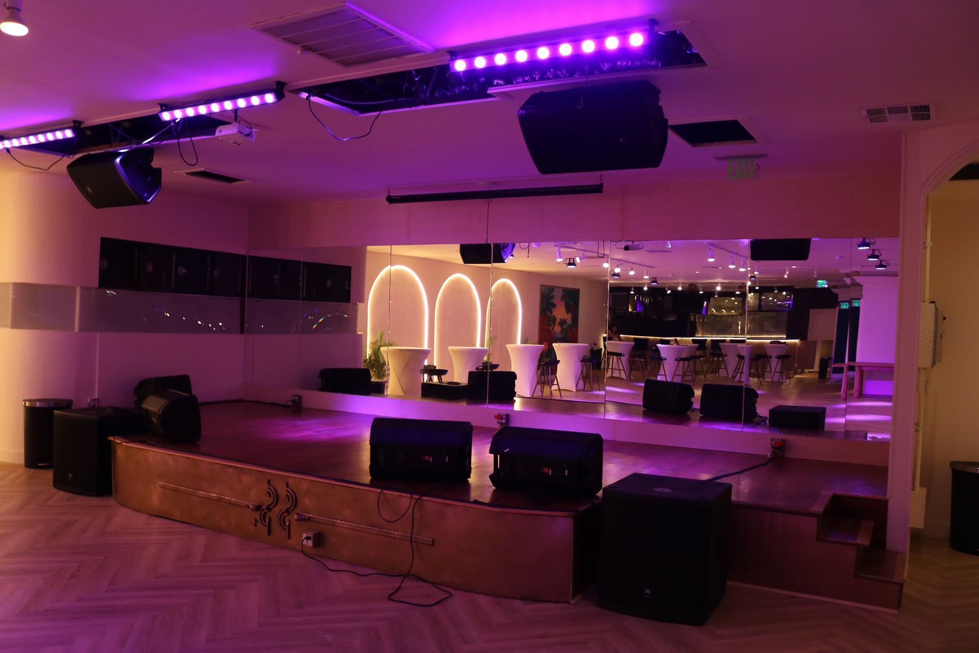 Purple-lit empty lounge with a stage, mirrored wall, and wooden floor