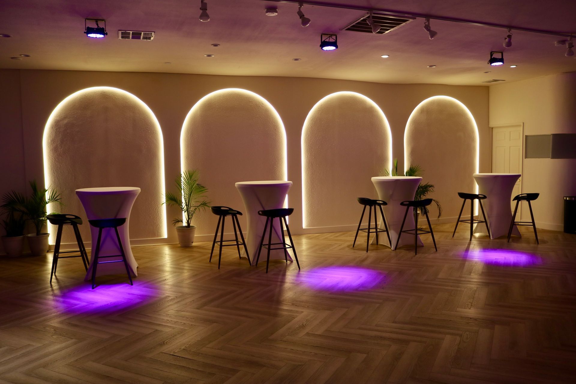 Dim lounge with purple-lit cocktail tables and arched alcoves in a warm, modern event space