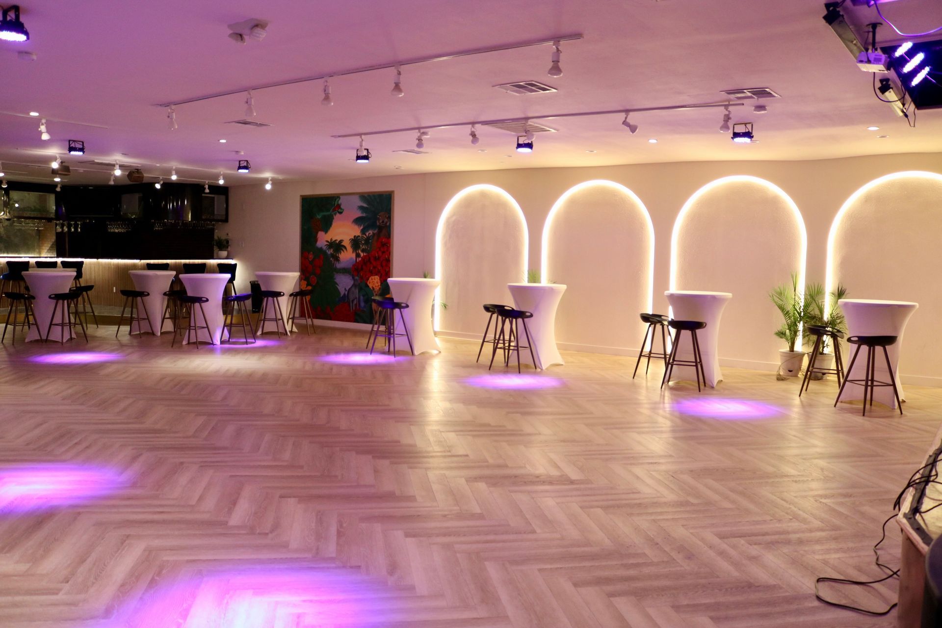 Empty event hall with warm arch lights, small cocktail tables, and purple accent lighting on a herringbone floor