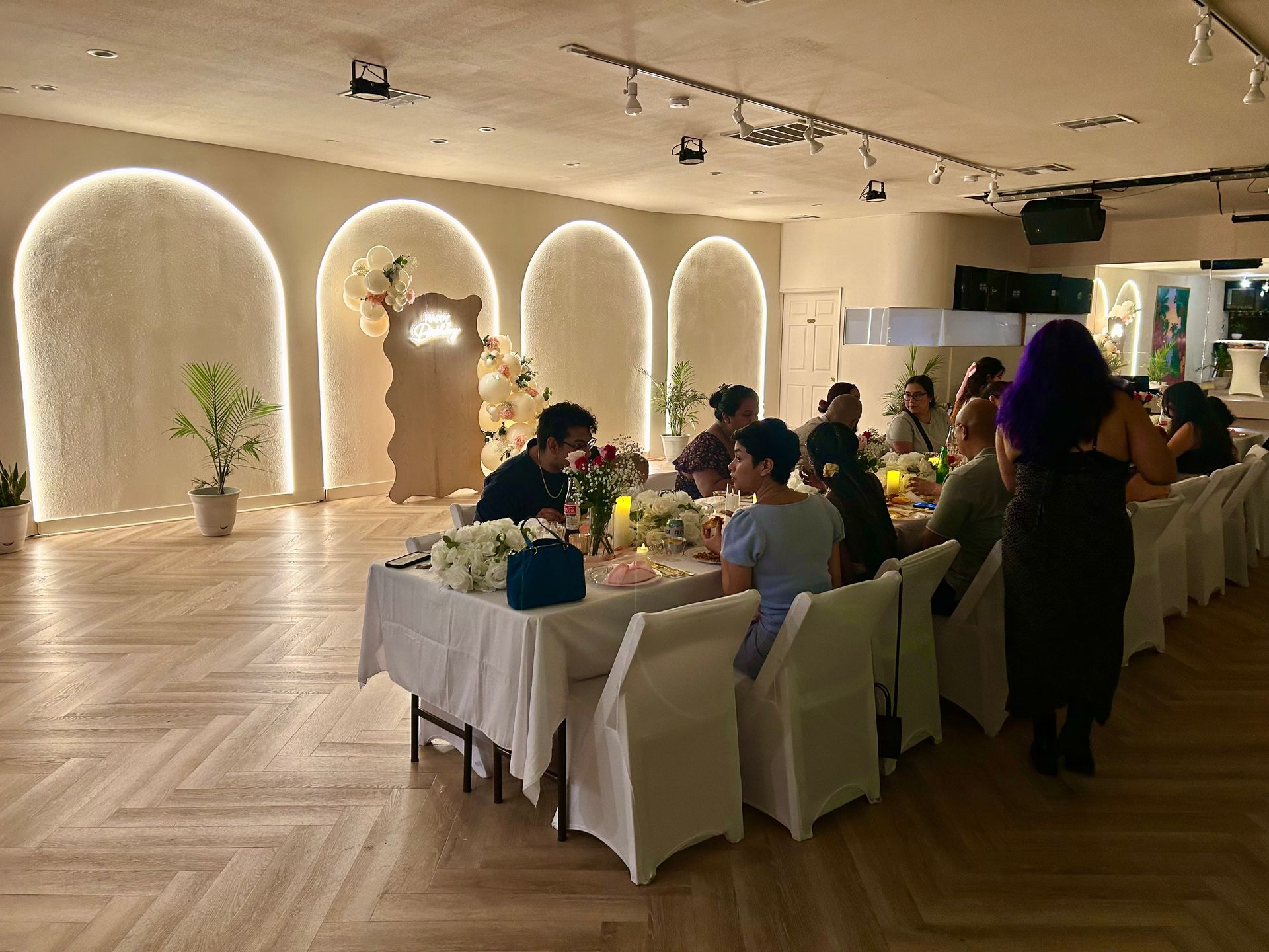 Guests seated at a long white-clothed table in a warmly lit banquet hall with arched wall lights