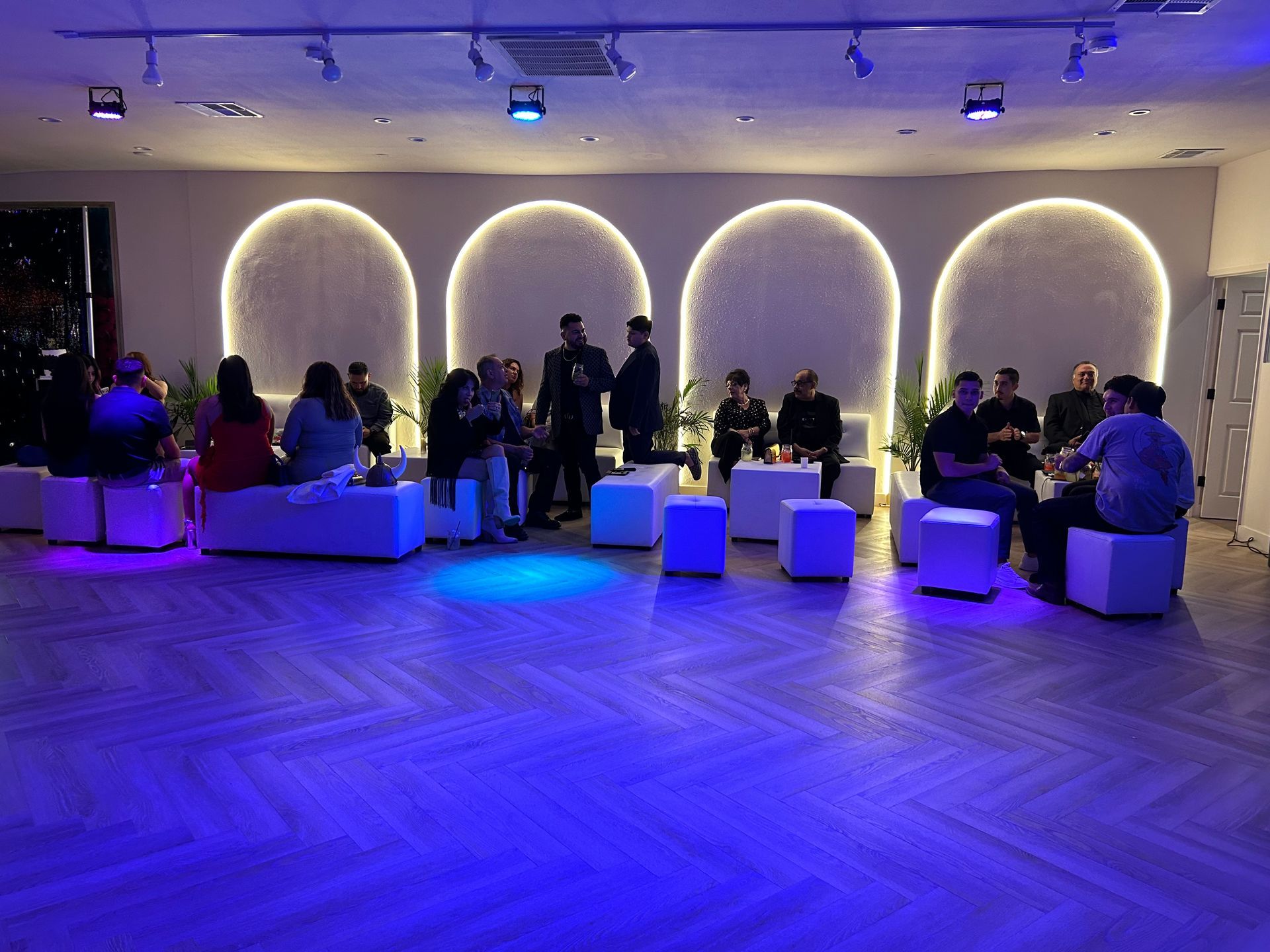 People seated in a blue-lit lounge with glowing wall arches and white cube stools